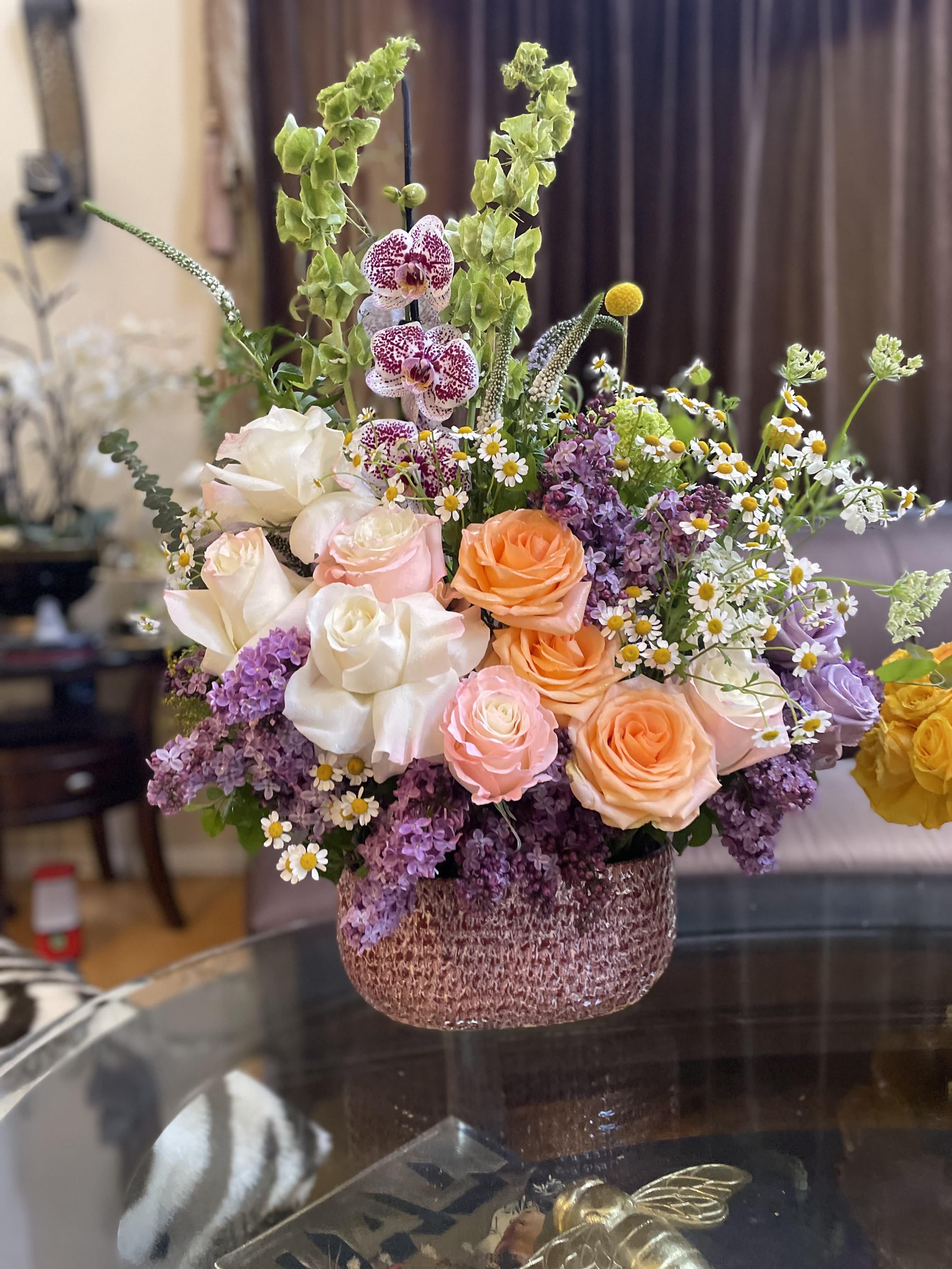Mixed bouquet of roses, orchids, and small daisies in a textured vase