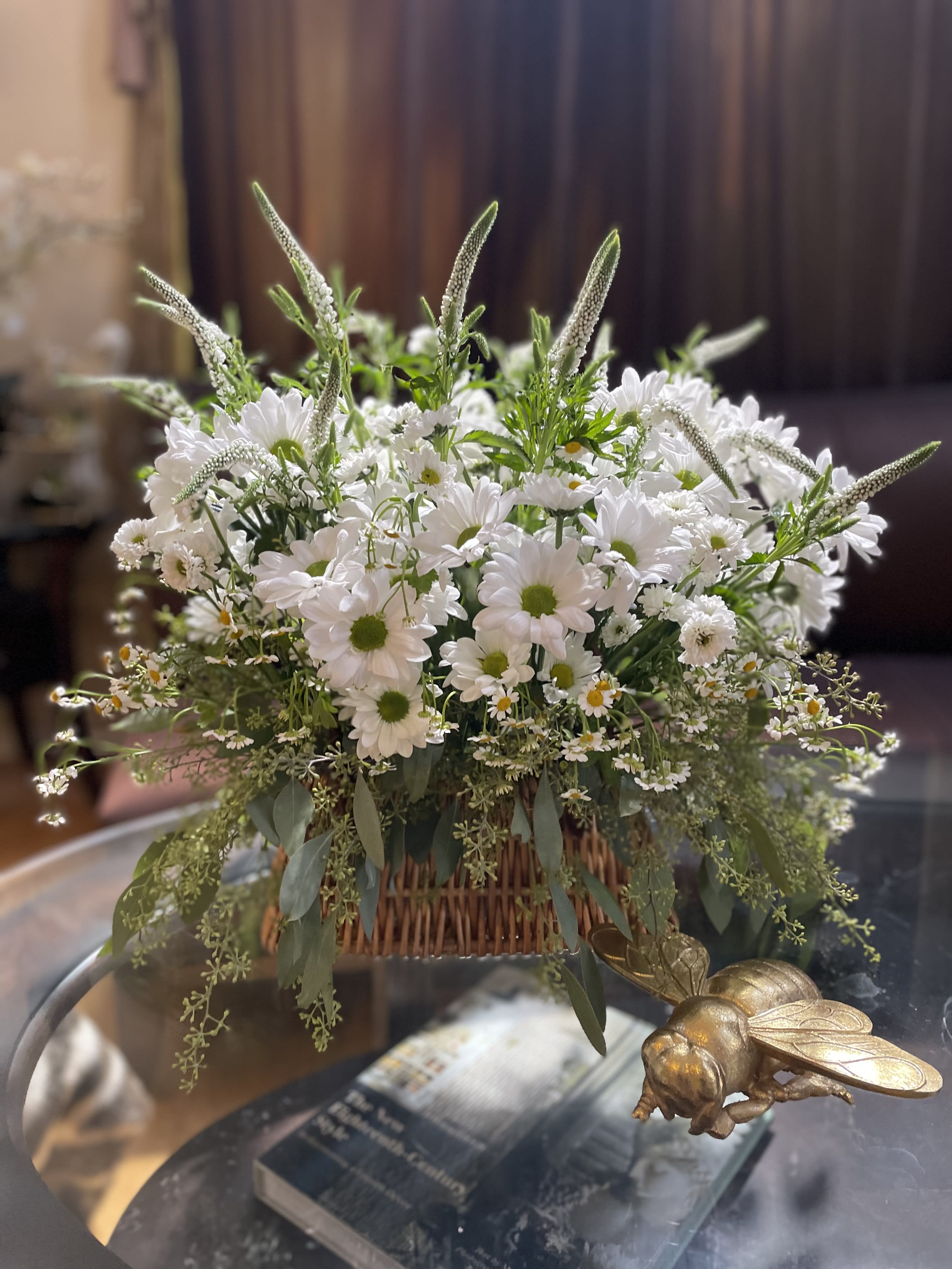 White daisy bouquet in a wicker basket with trailing greenery