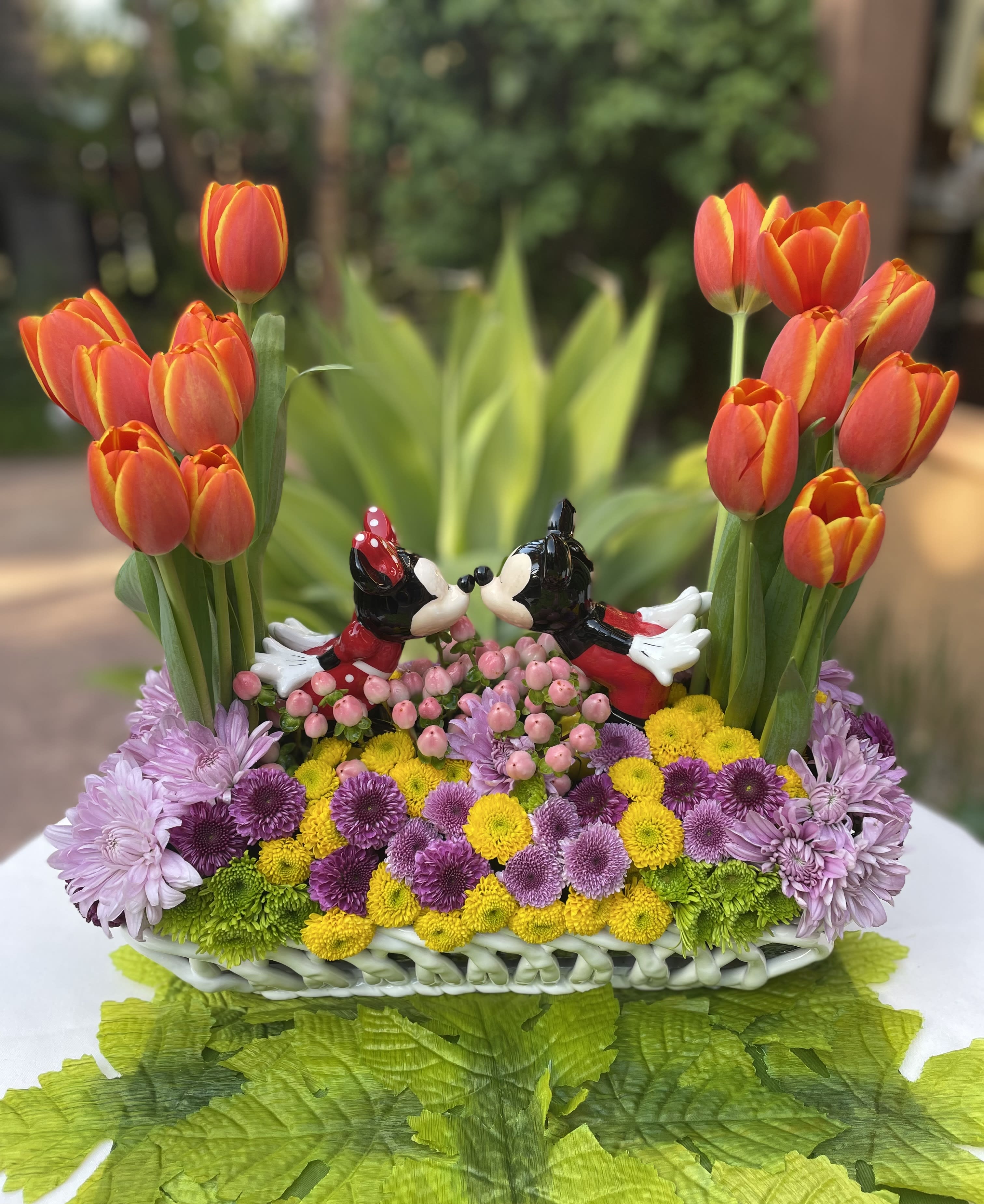 Basket arrangement with orange tulips and colorful mums featuring Mickey and Minnie figurines