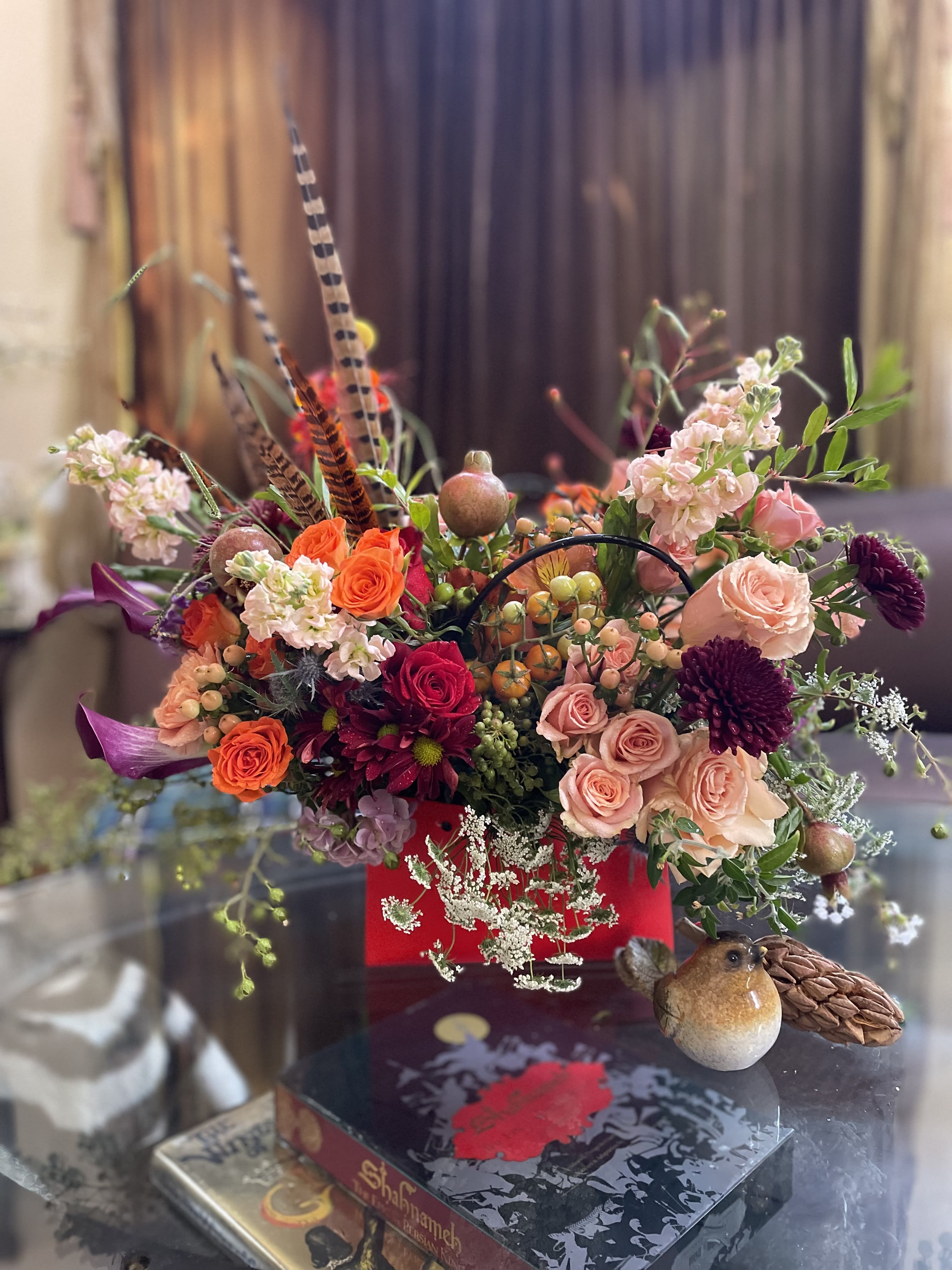 Mixed bouquet with roses, chrysanthemums, and decorative bird accents in a red container