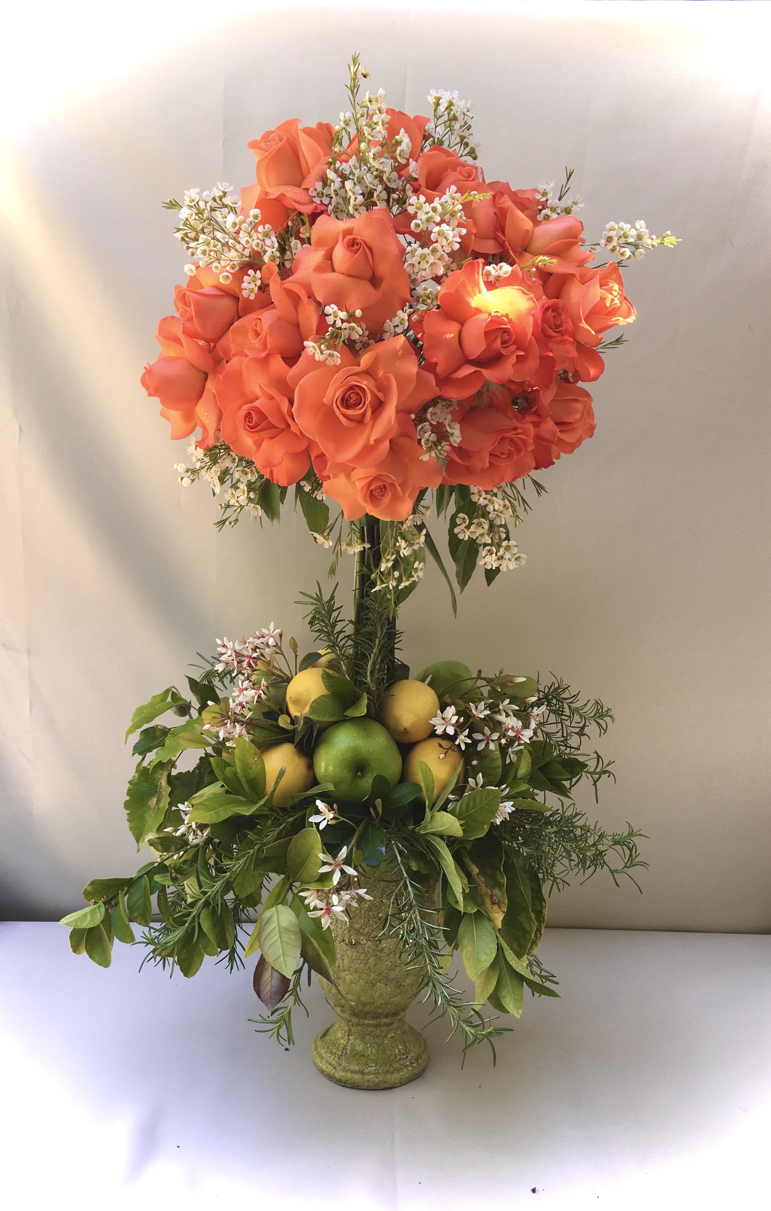 Orange roses in a tall vase with lemons and greenery