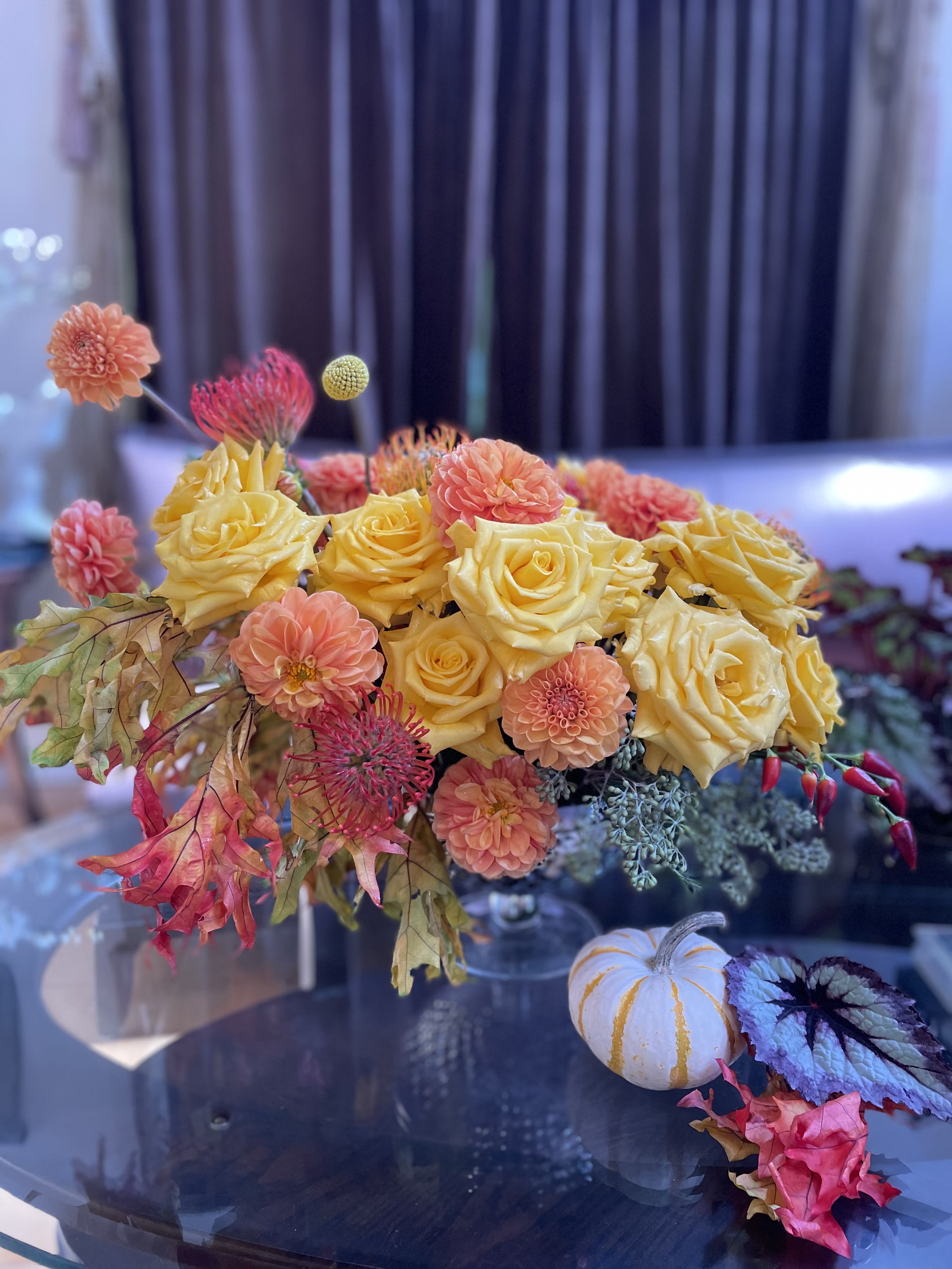 Yellow roses and peach dahlias in a low arrangement with autumn leaves