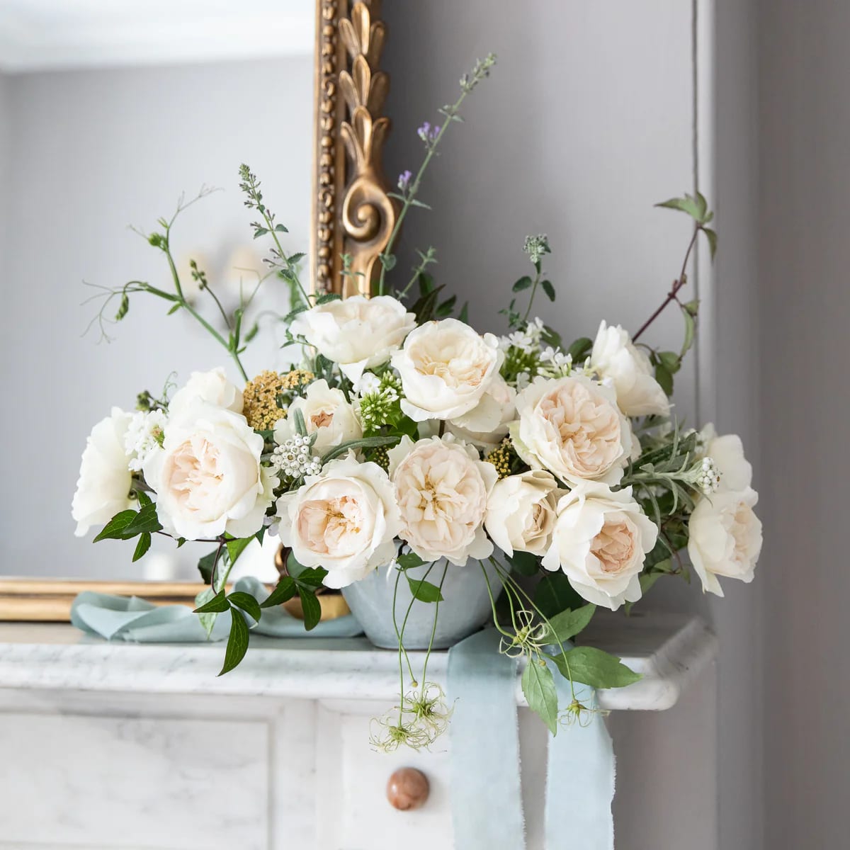Cream roses arranged in a pale blue vase on a mantel
