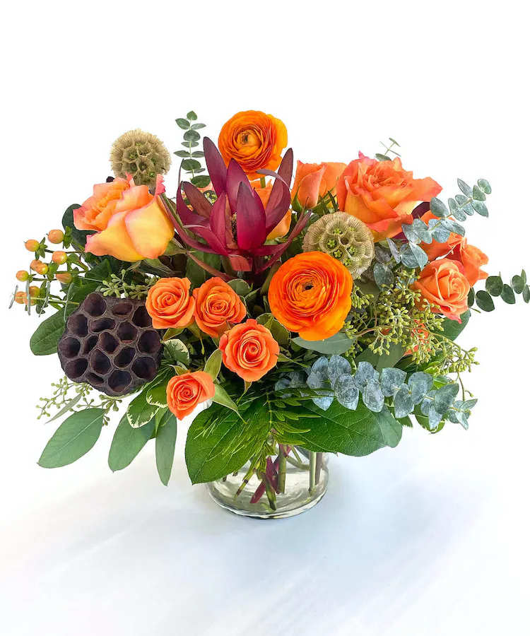 Orange roses and ranunculus in a glass vase with mixed greenery