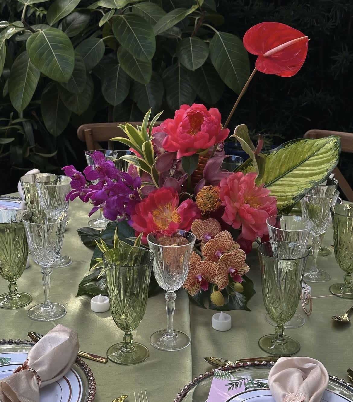 Tropical floral centerpiece with pink and purple blooms on a table set with glassware