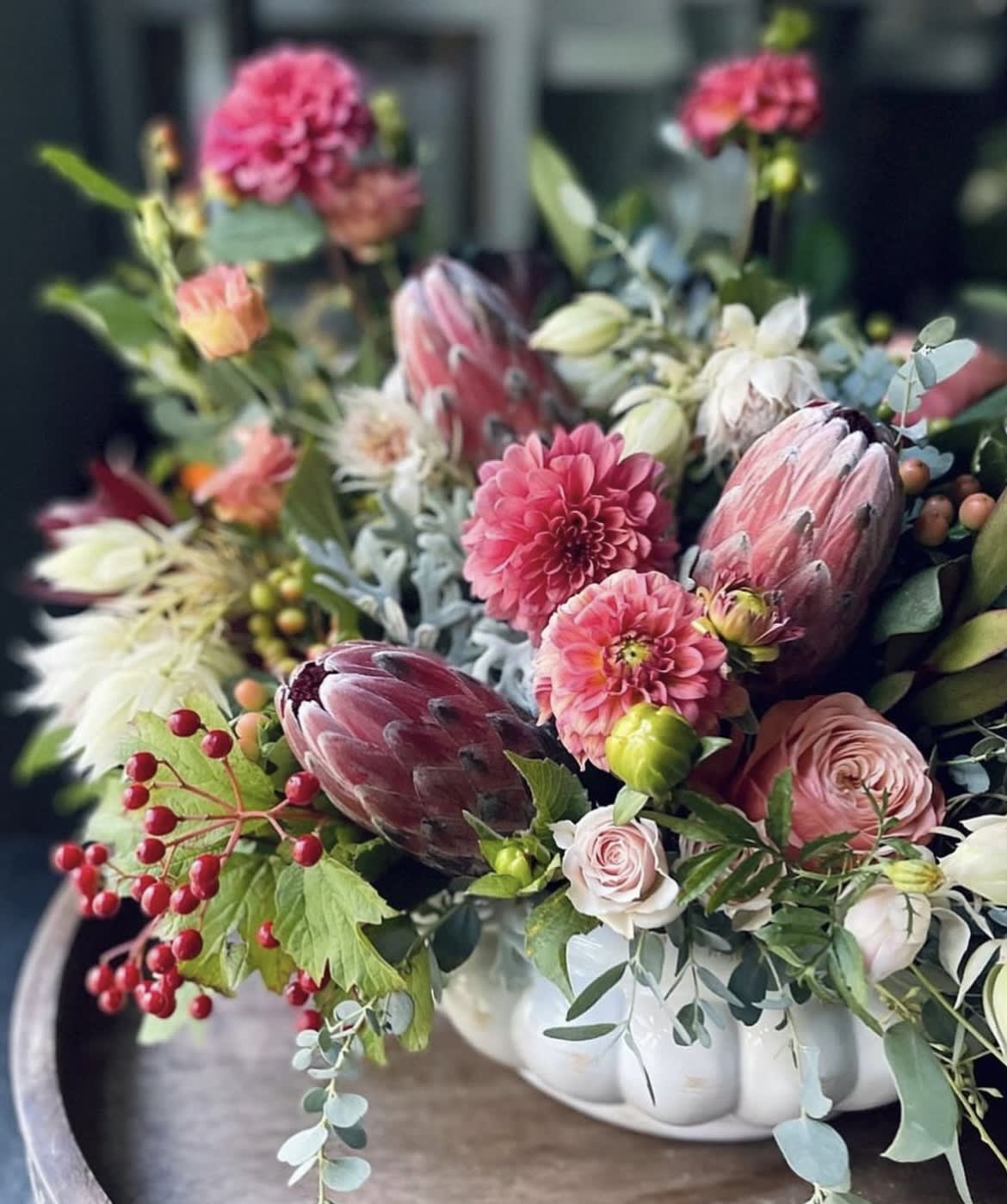 Mixed bouquet with pink blooms and protea in a white vase