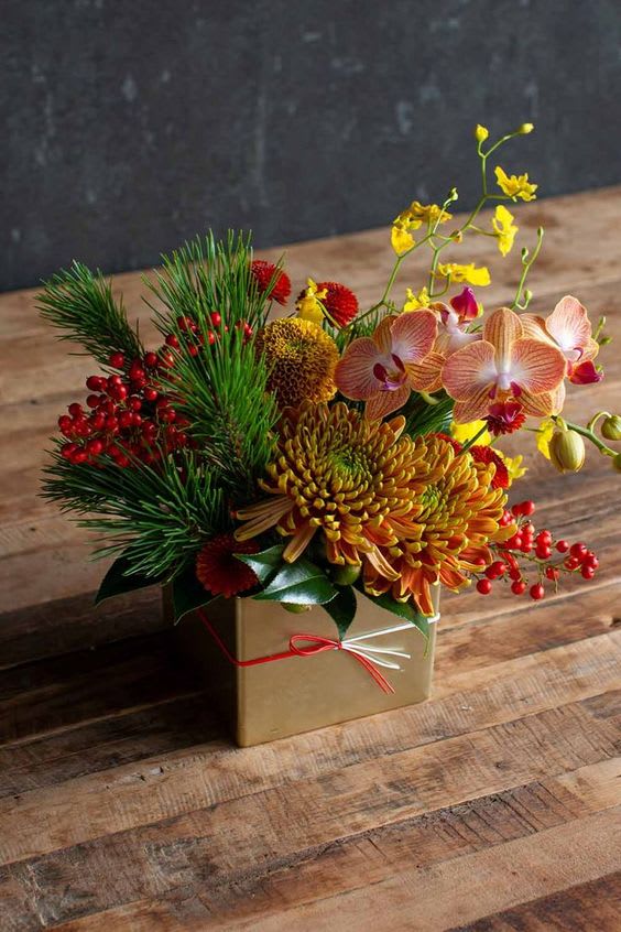 Mixed floral arrangement in a gold box with orchids and red berries