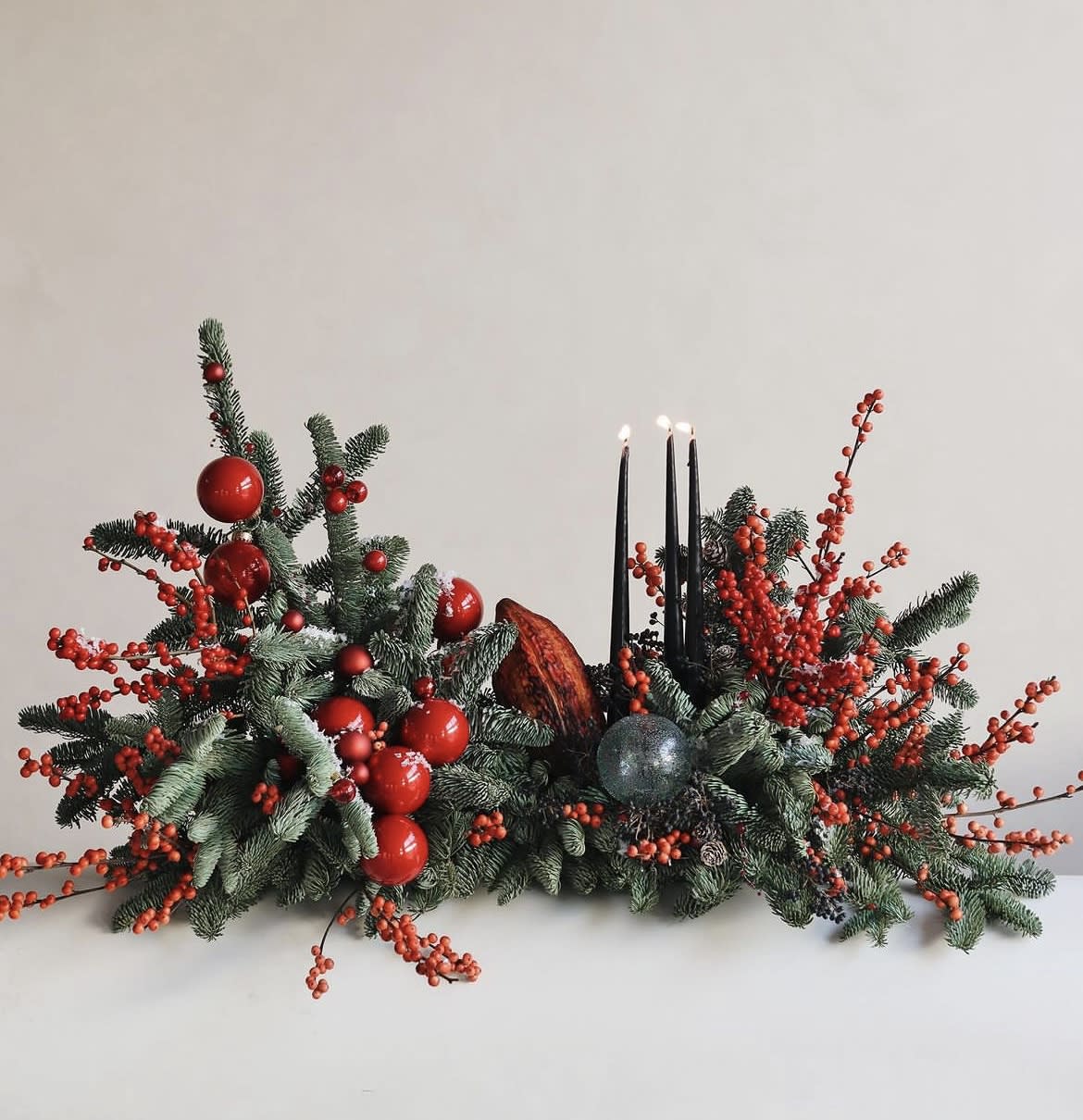 Low holiday centerpiece with evergreen branches, red berries, and black candles