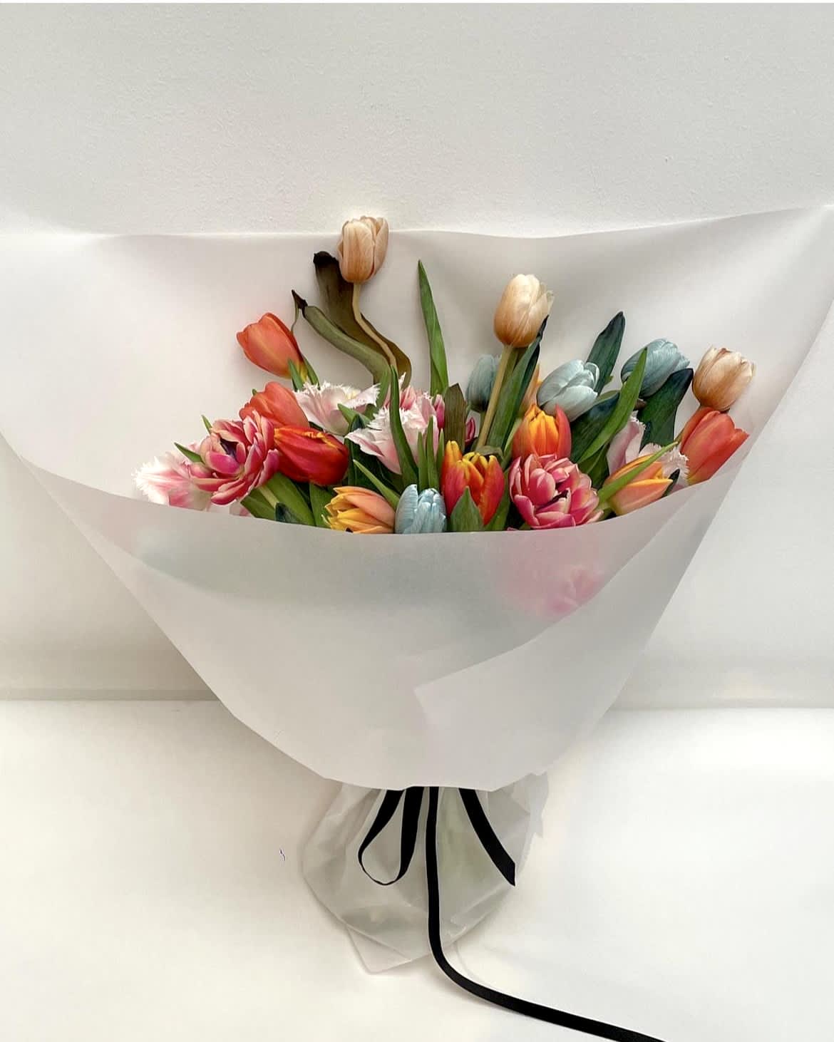 Mixed tulip bouquet wrapped in white paper with a black ribbon