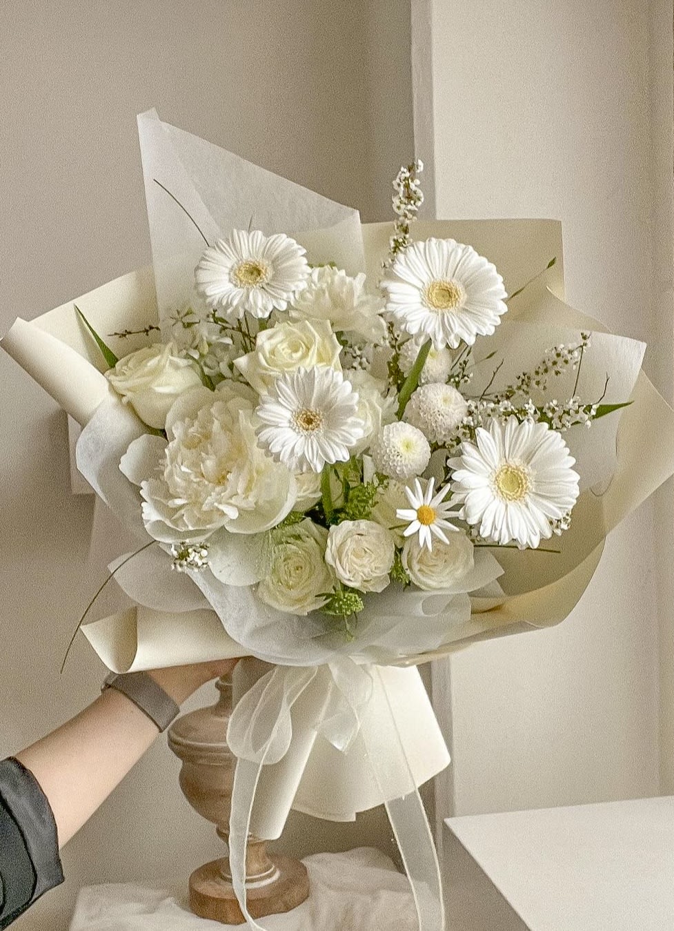 White bouquet with gerbera daisies and roses wrapped in cream paper