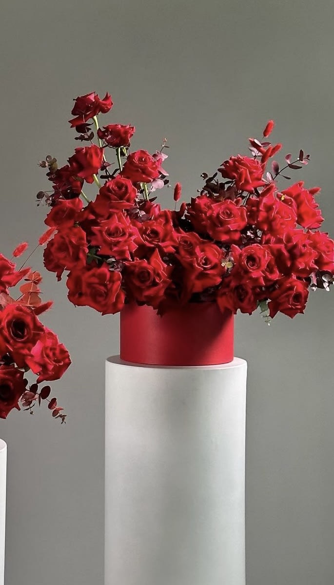 Red rose arrangement in a red cylindrical vase on a white pedestal