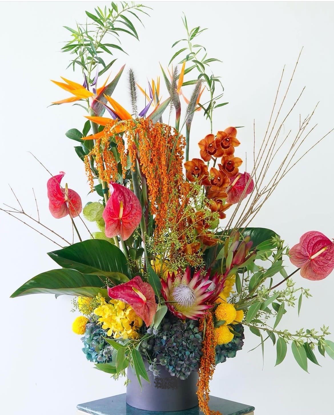 Tall tropical floral arrangement with orange birds of paradise and pink anthuriums in a vase