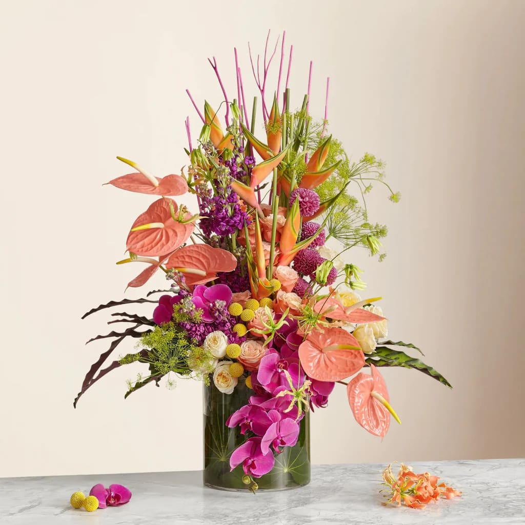 Tall tropical bouquet in a glass vase with pink and orange blooms