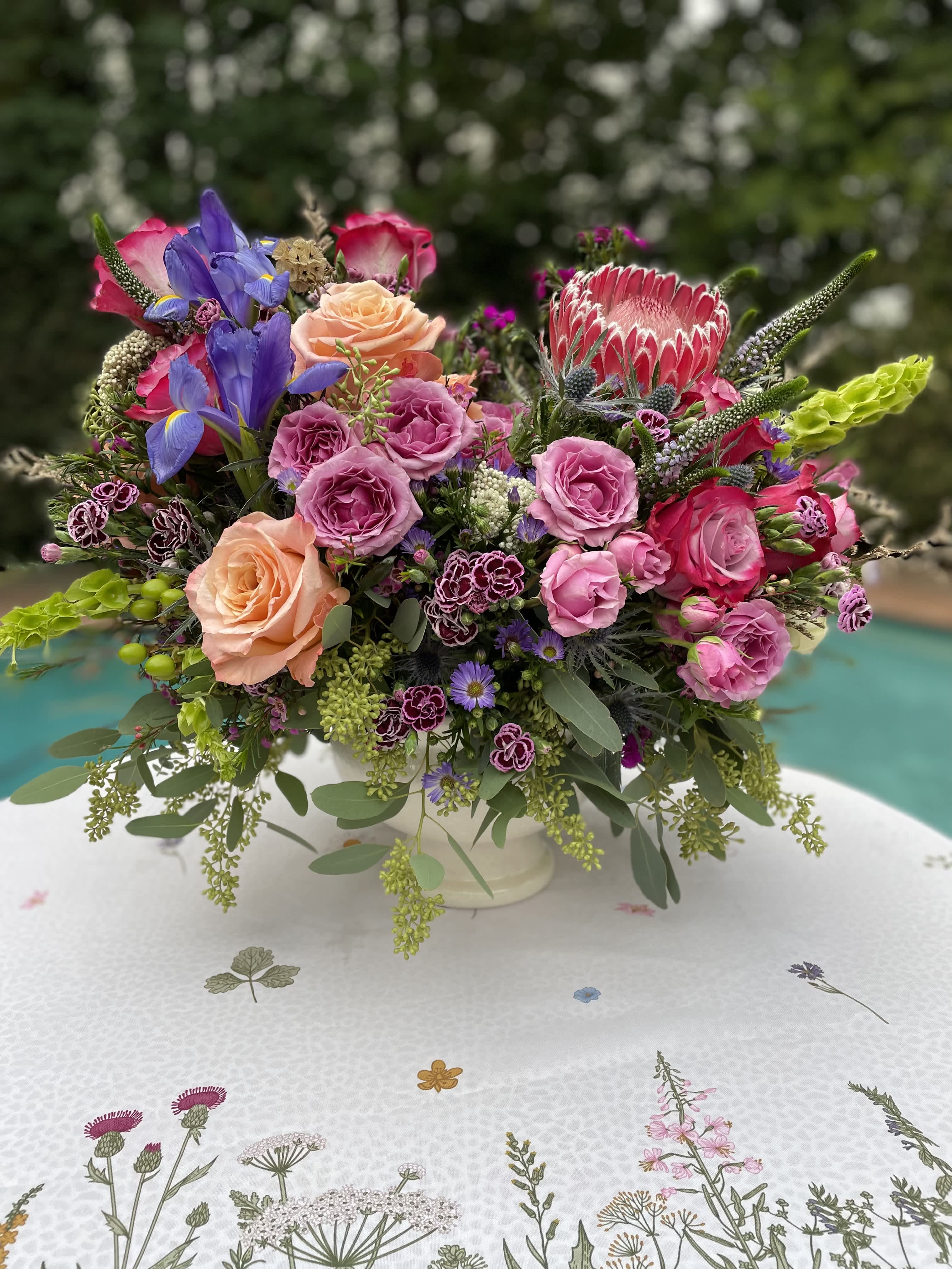Colorful mixed flower arrangement in a white vase on a patterned tablecloth