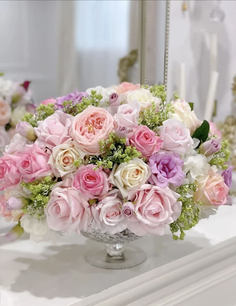 Pastel pink and lavender roses arranged in a clear pedestal vase