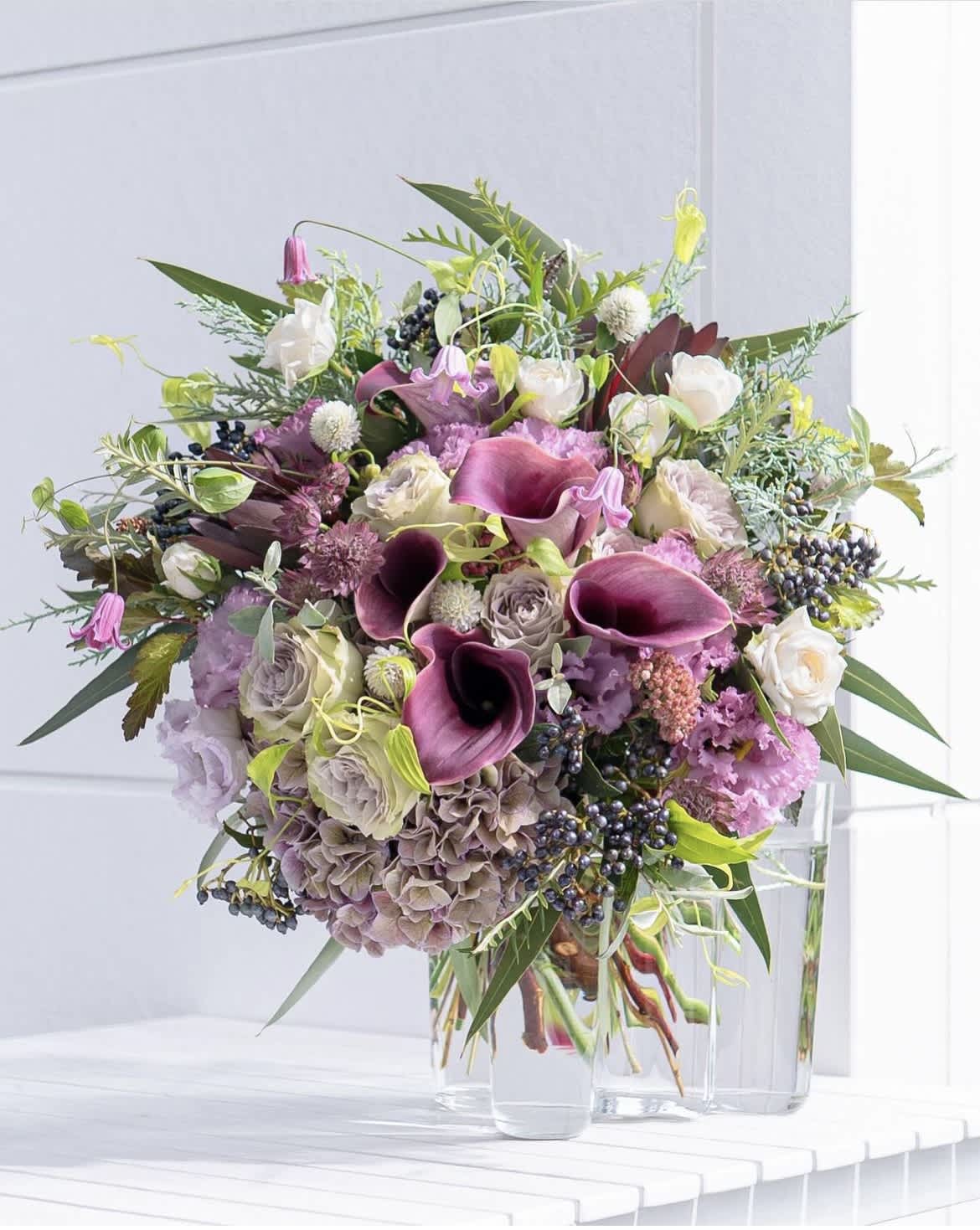 Bouquet of purple calla lilies, roses, and hydrangeas in a clear glass vase