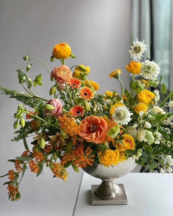 Mixed orange, yellow, white, and peach flowers in a silver pedestal vase