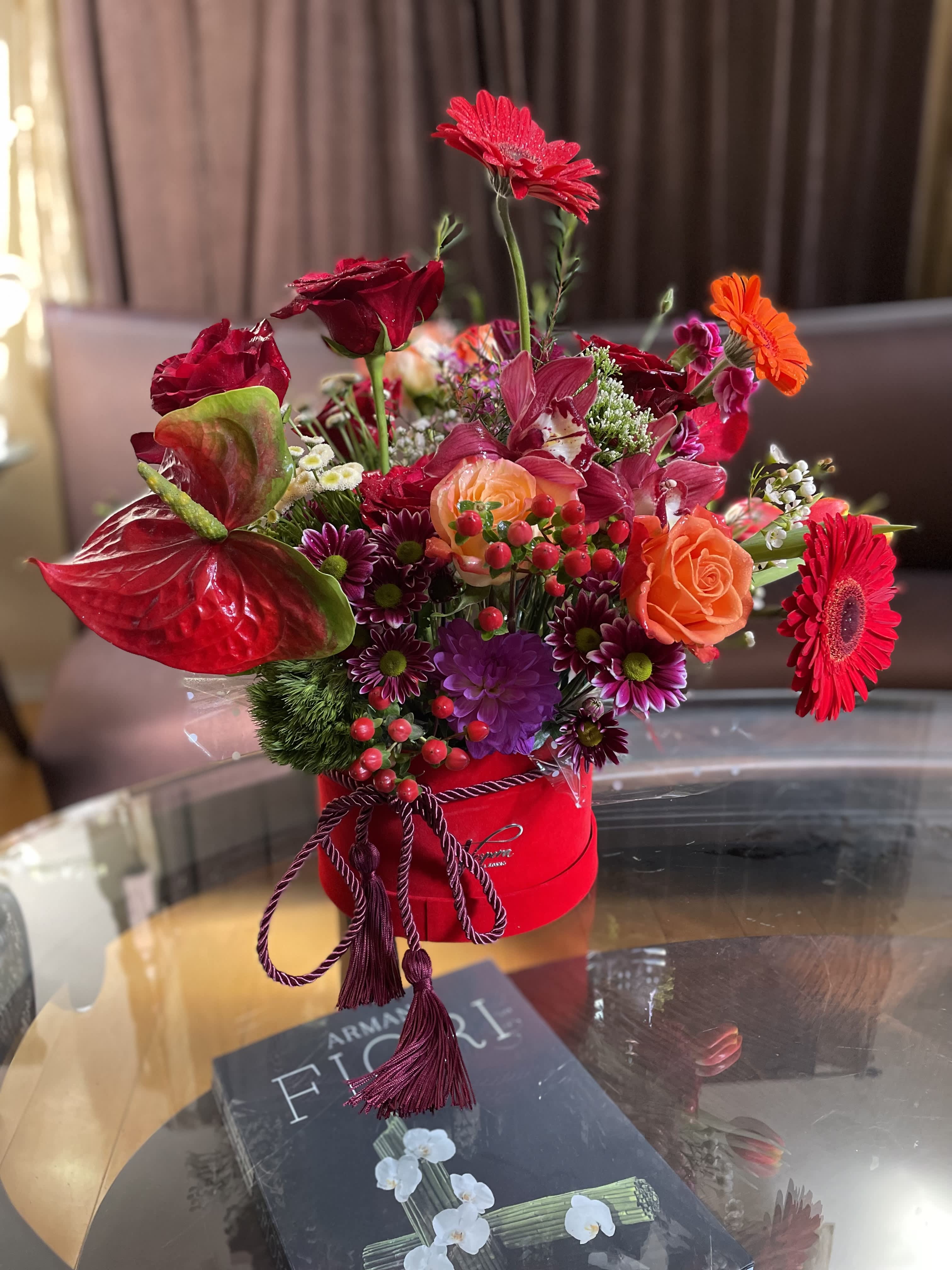 Bright mixed flower arrangement in a red hat box with roses and gerbera daisies