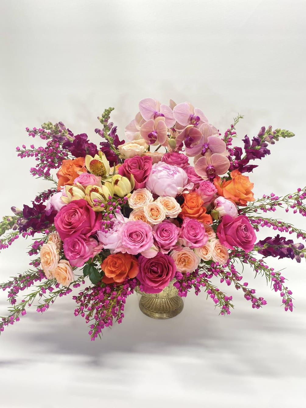 Large bouquet of pink and orange roses with orchids in a gold vase