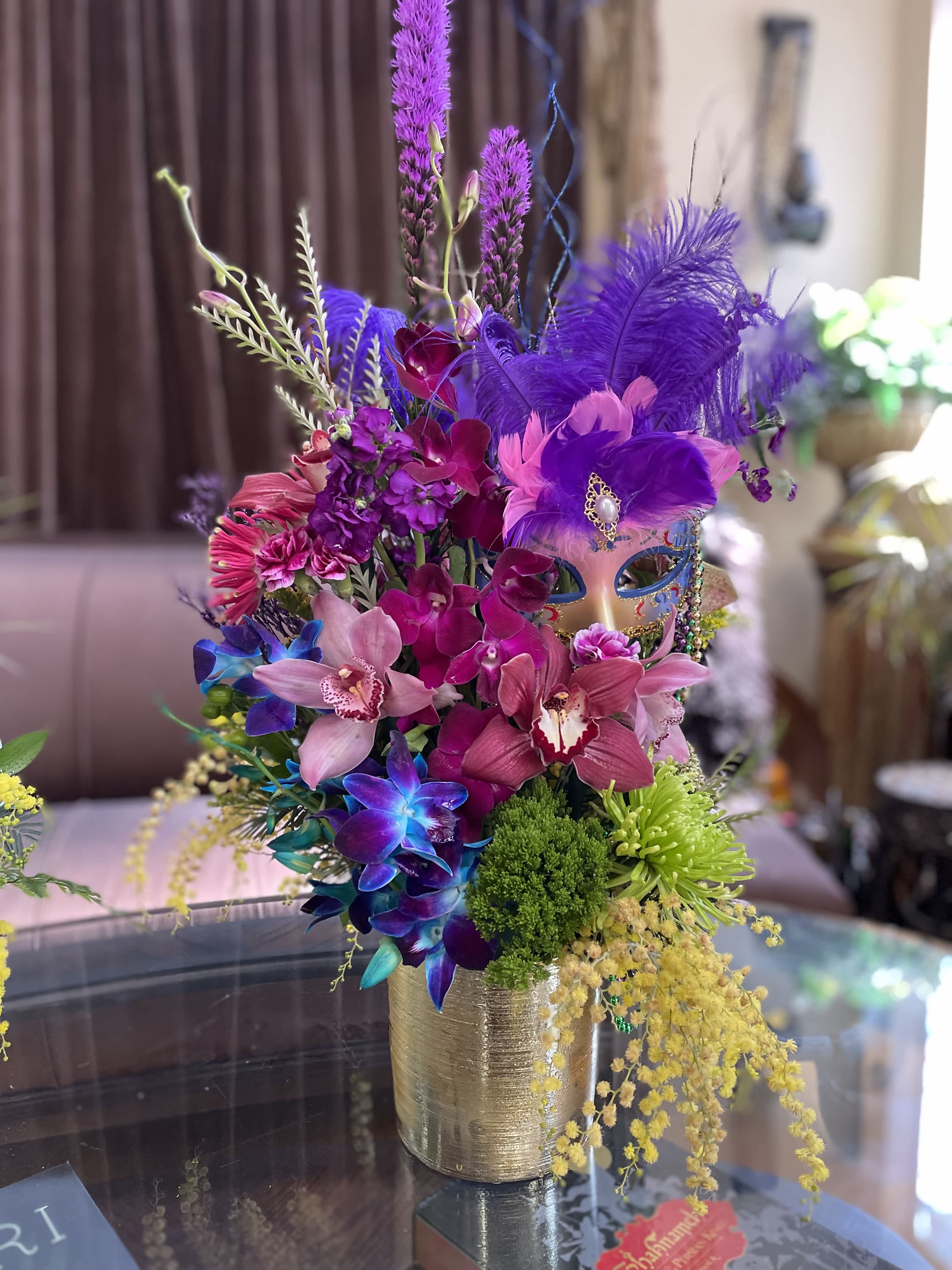 Colorful bouquet with orchids, feathers, and a decorative mask in a gold vase