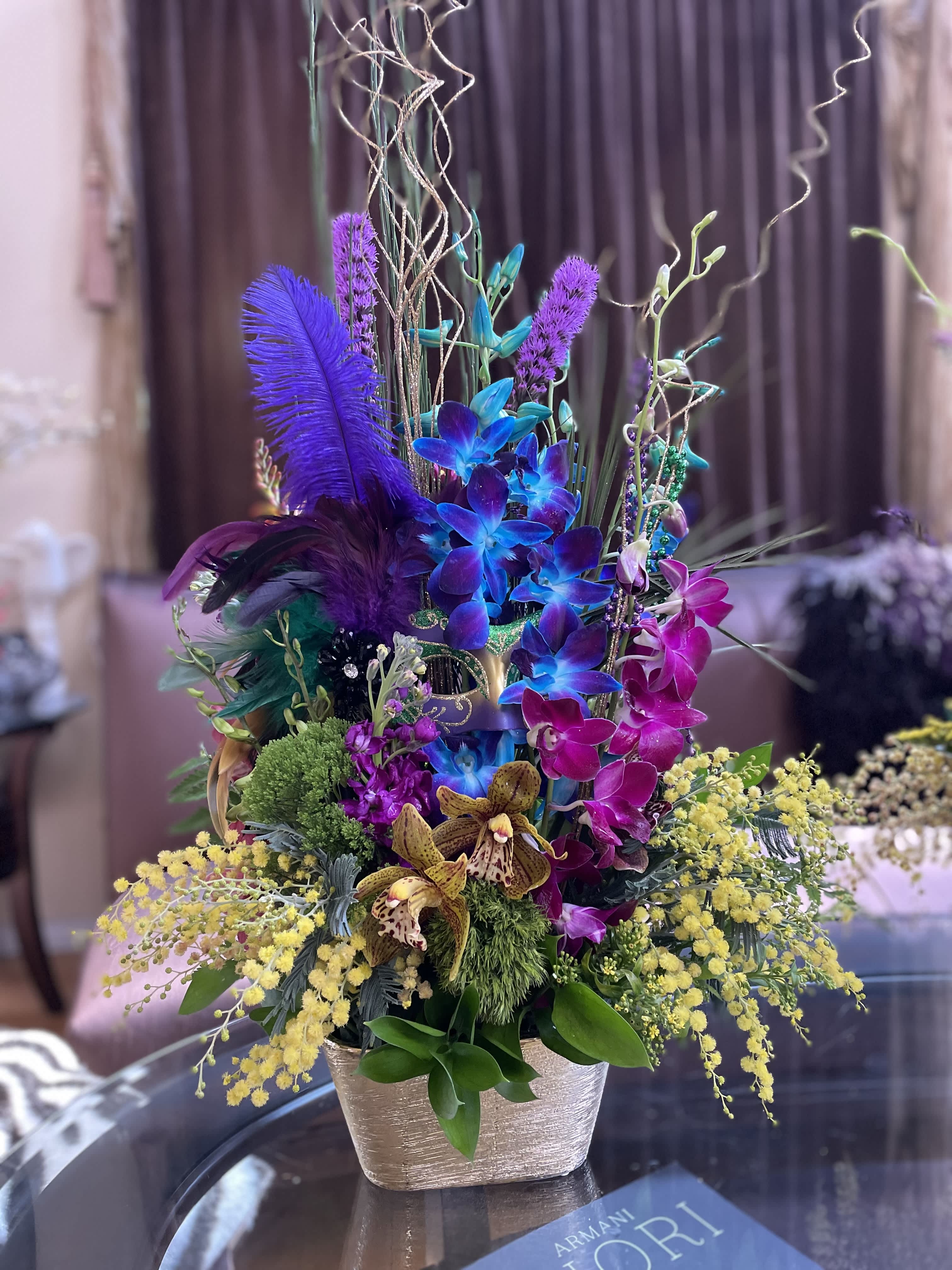 Tall colorful floral arrangement in a gold vase with orchids and feathers
