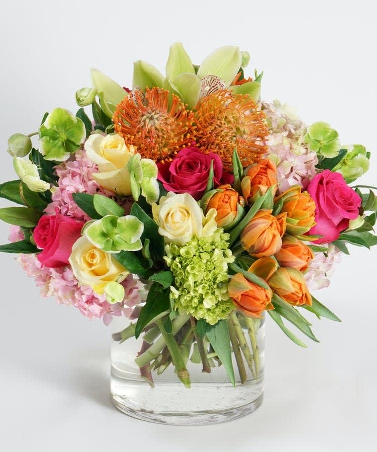 Mixed bouquet of roses, hydrangeas, and orange blooms in a glass vase