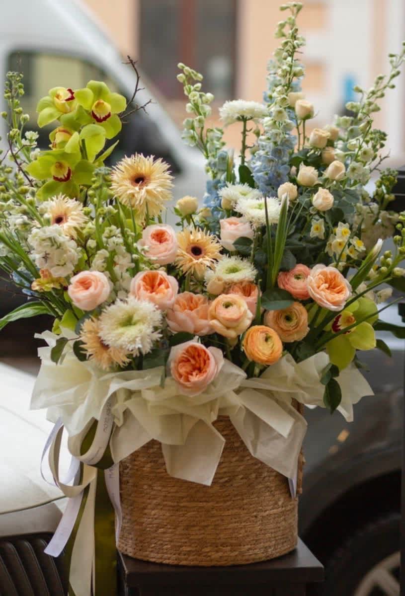 Mixed bouquet in a woven basket with peach, white, blue, and green flowers