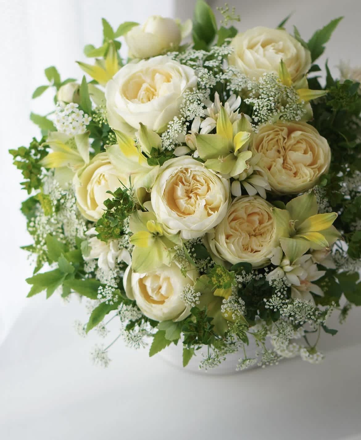 Cream roses and white flowers arranged in a white vase