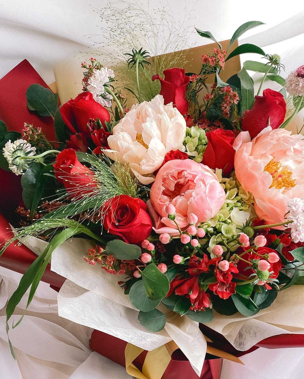 Bouquet of red and blush flowers wrapped in white paper