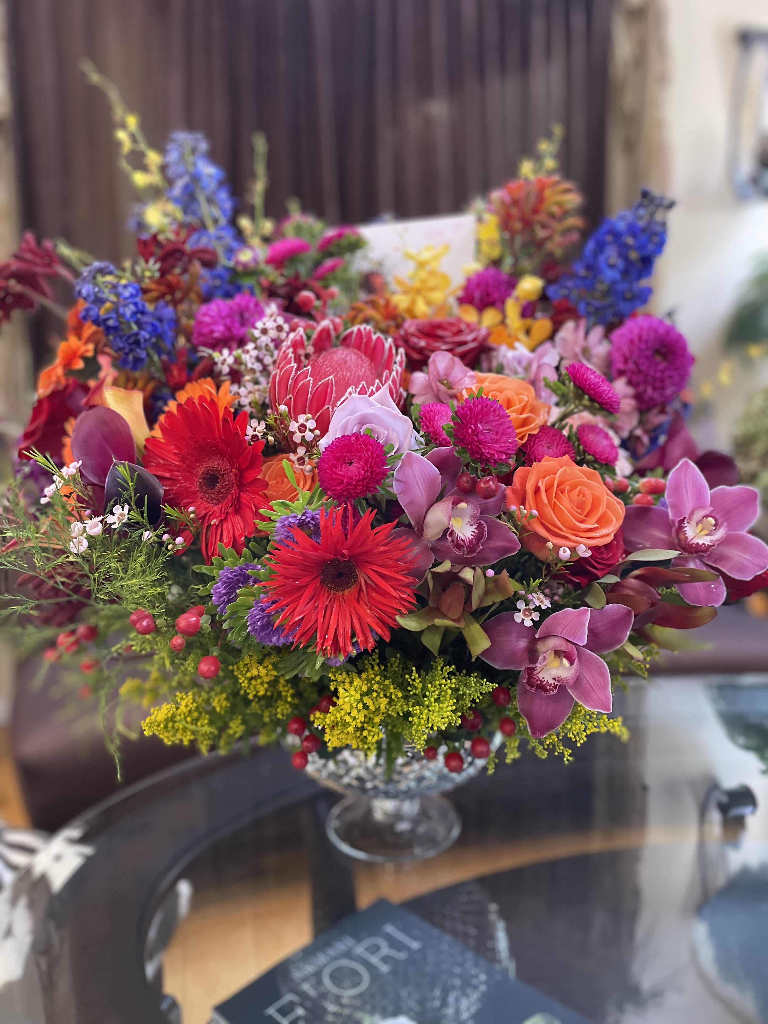 Colorful mixed bouquet with roses, orchids, and gerbera daisies in a glass vase