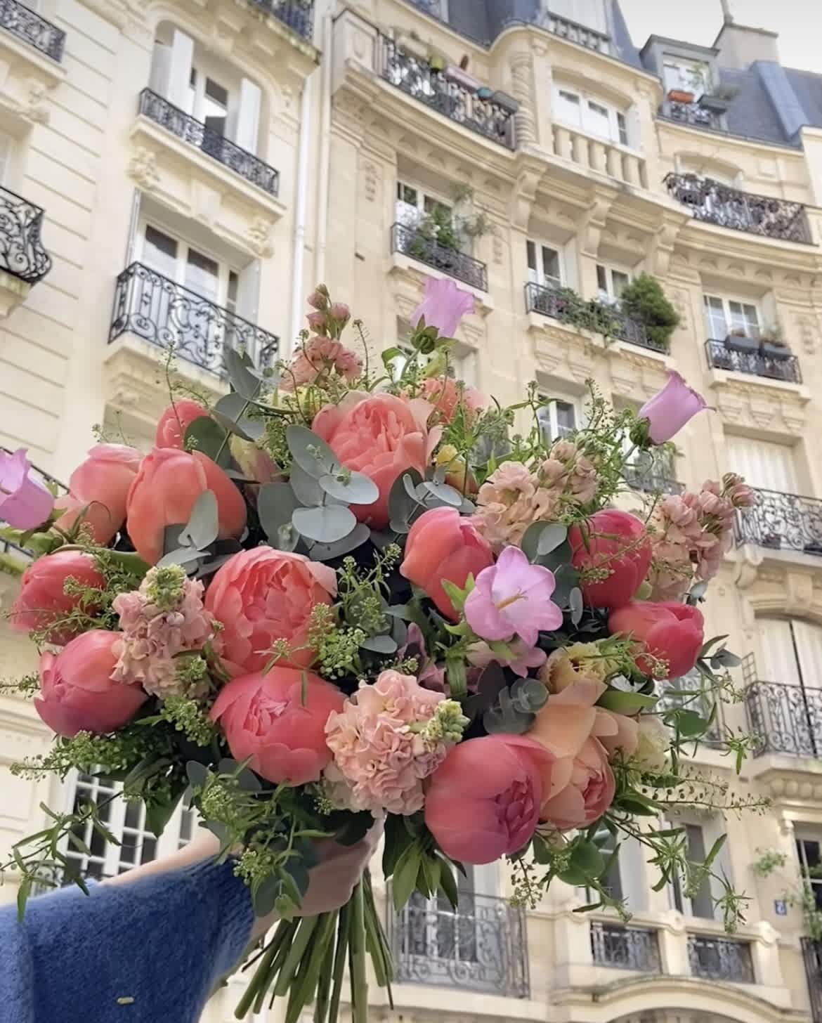 Pink and peach bouquet with tulips and roses held in front of a building
