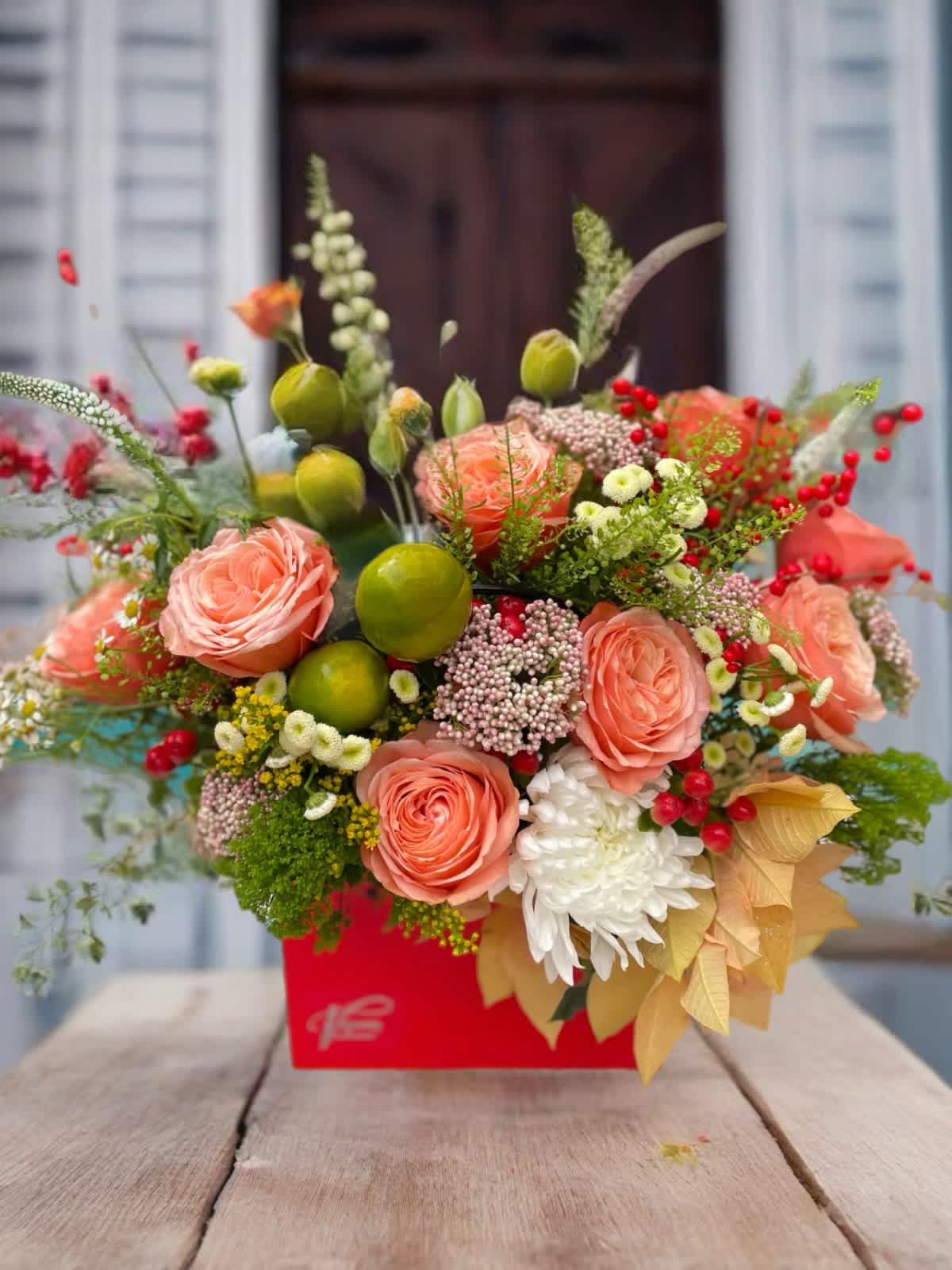 Peach roses and mixed blooms arranged in a red box with berries