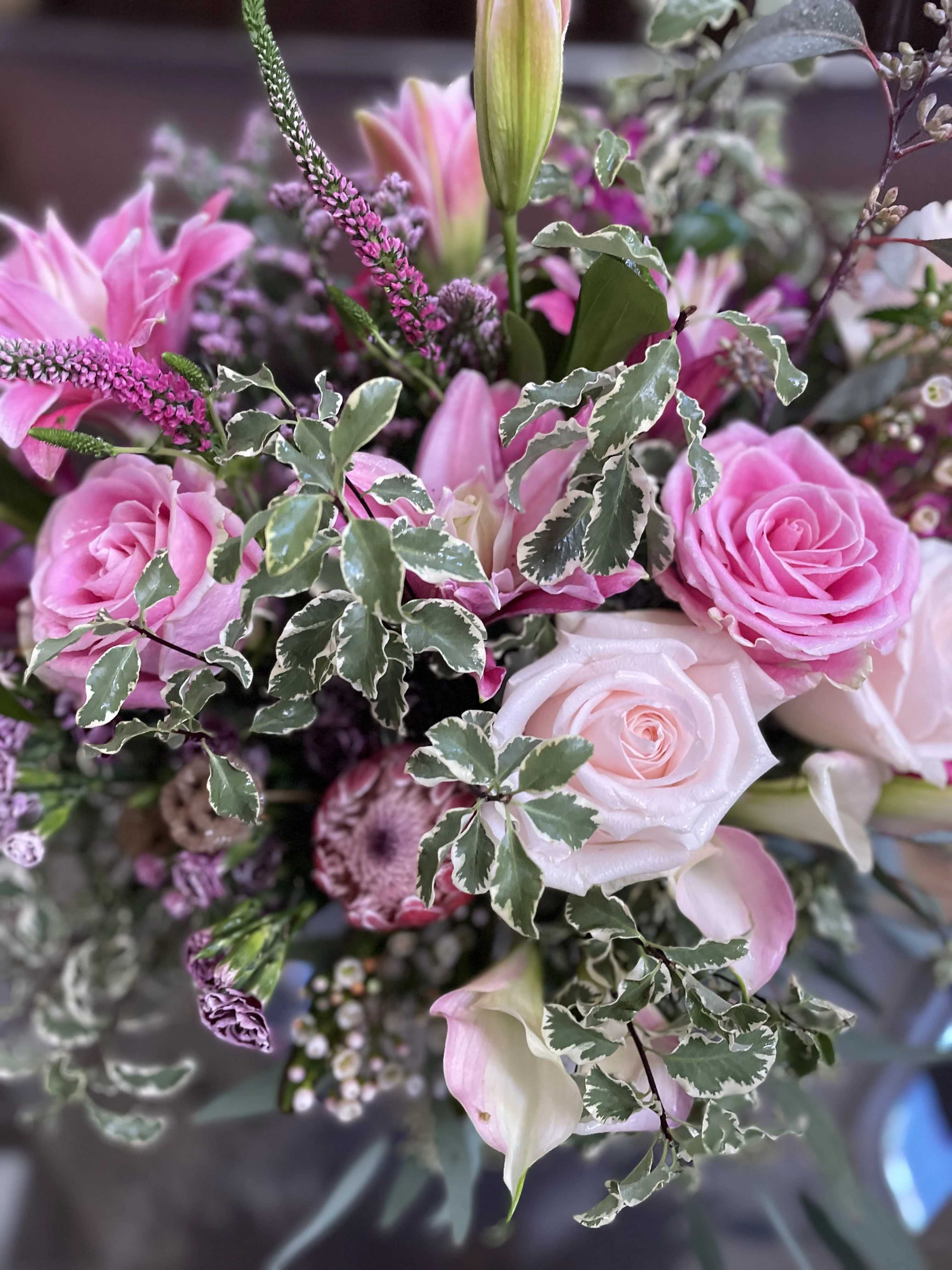 Pink roses and lilies arranged with variegated foliage.