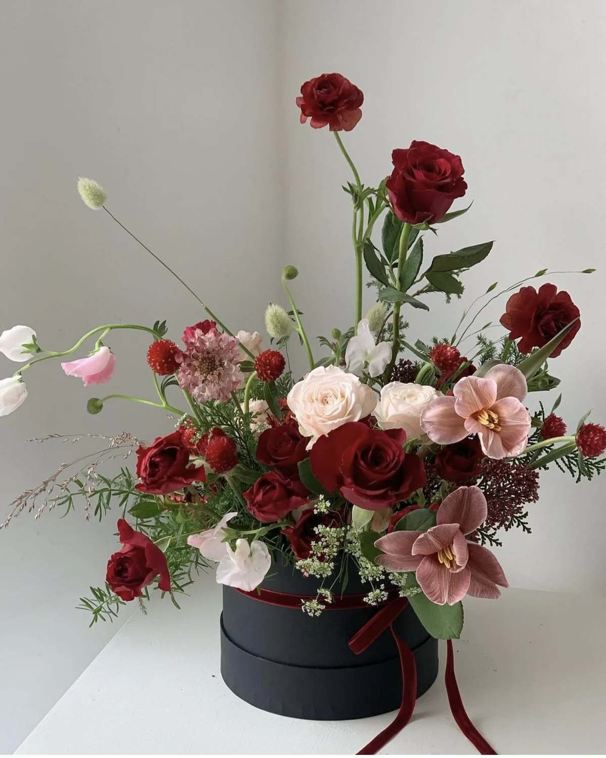 Red and blush floral arrangement in a black hat box with ribbon