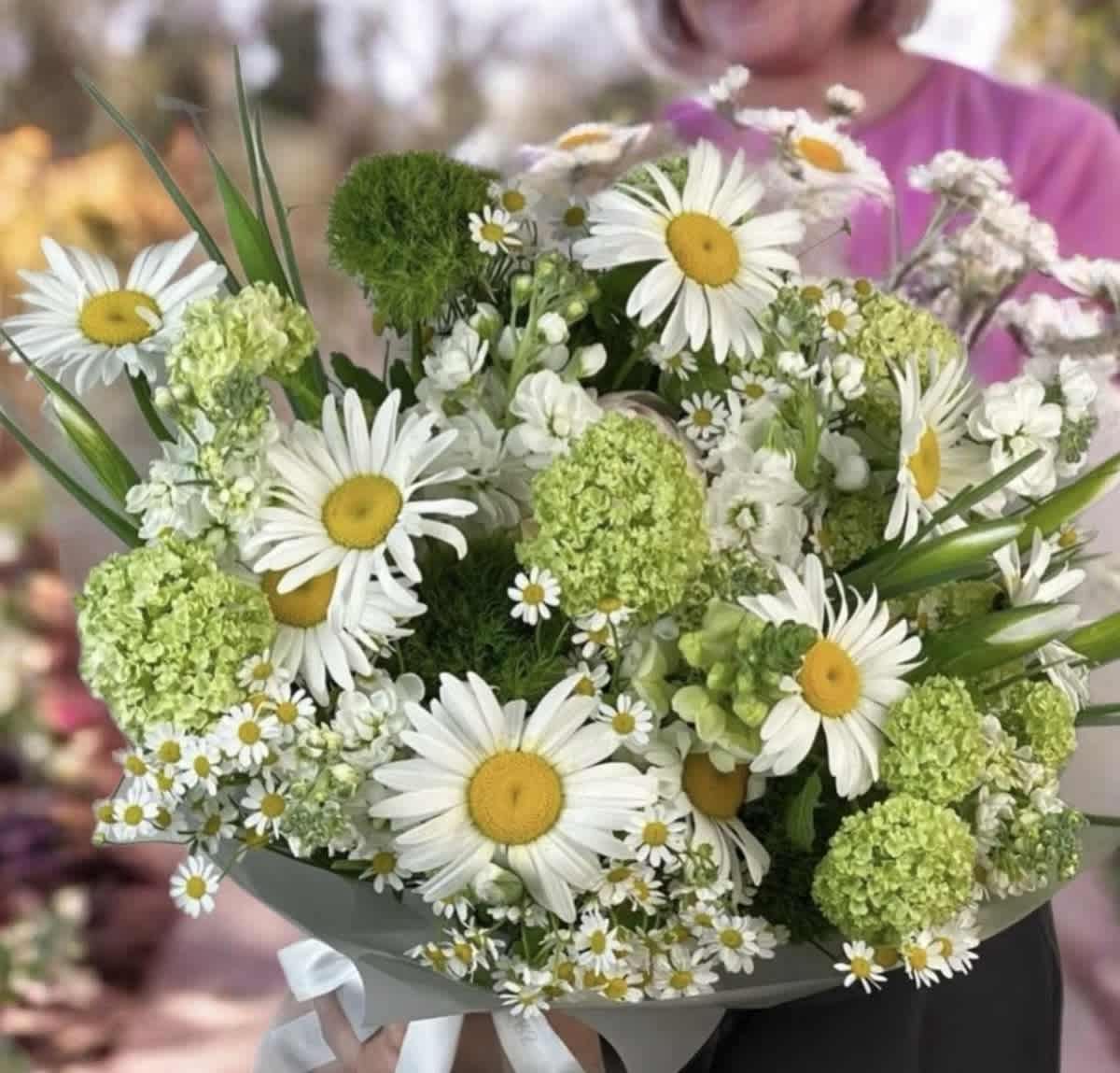 Bouquet of white daisies and green pom-pom flowers wrapped in gray paper