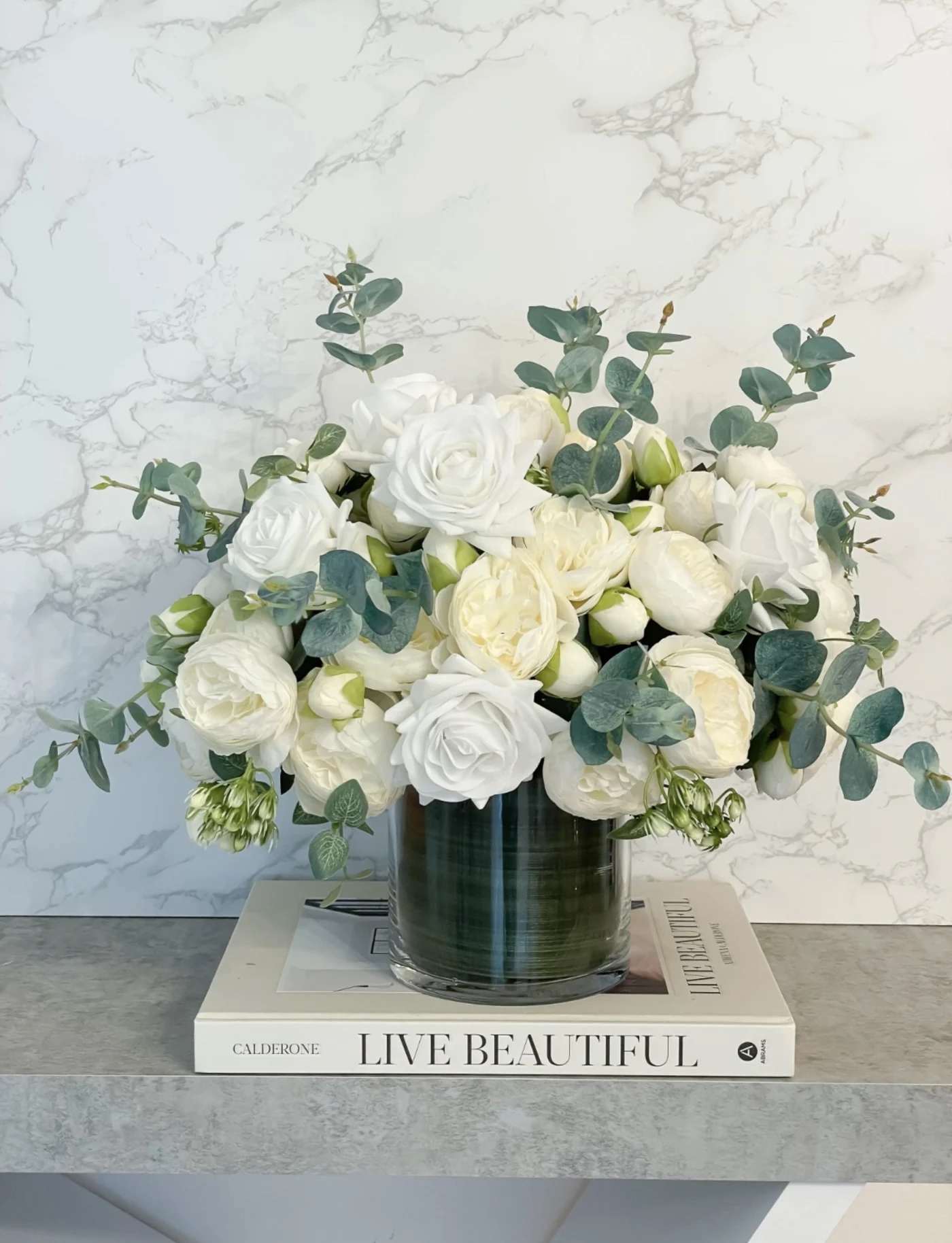 White roses and cream blooms in a glass vase with eucalyptus