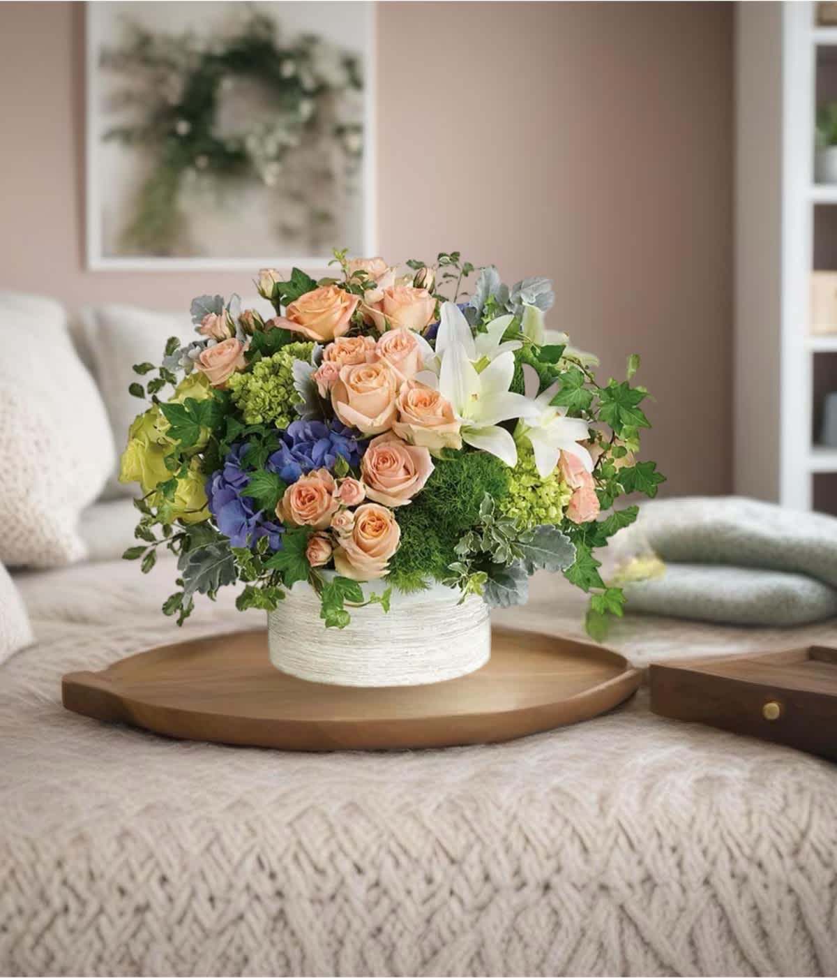 Mixed bouquet of peach roses, white lilies, and blue hydrangeas in a white vase