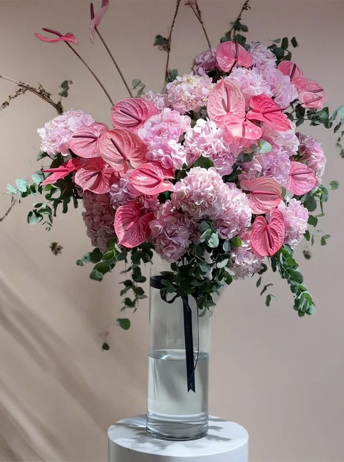 Pink hydrangea arrangement with anthuriums in a tall glass vase