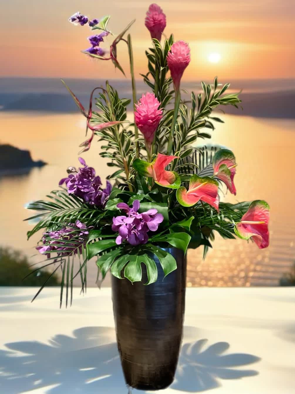 Tropical flower arrangement in a tall dark vase with pink and purple blooms