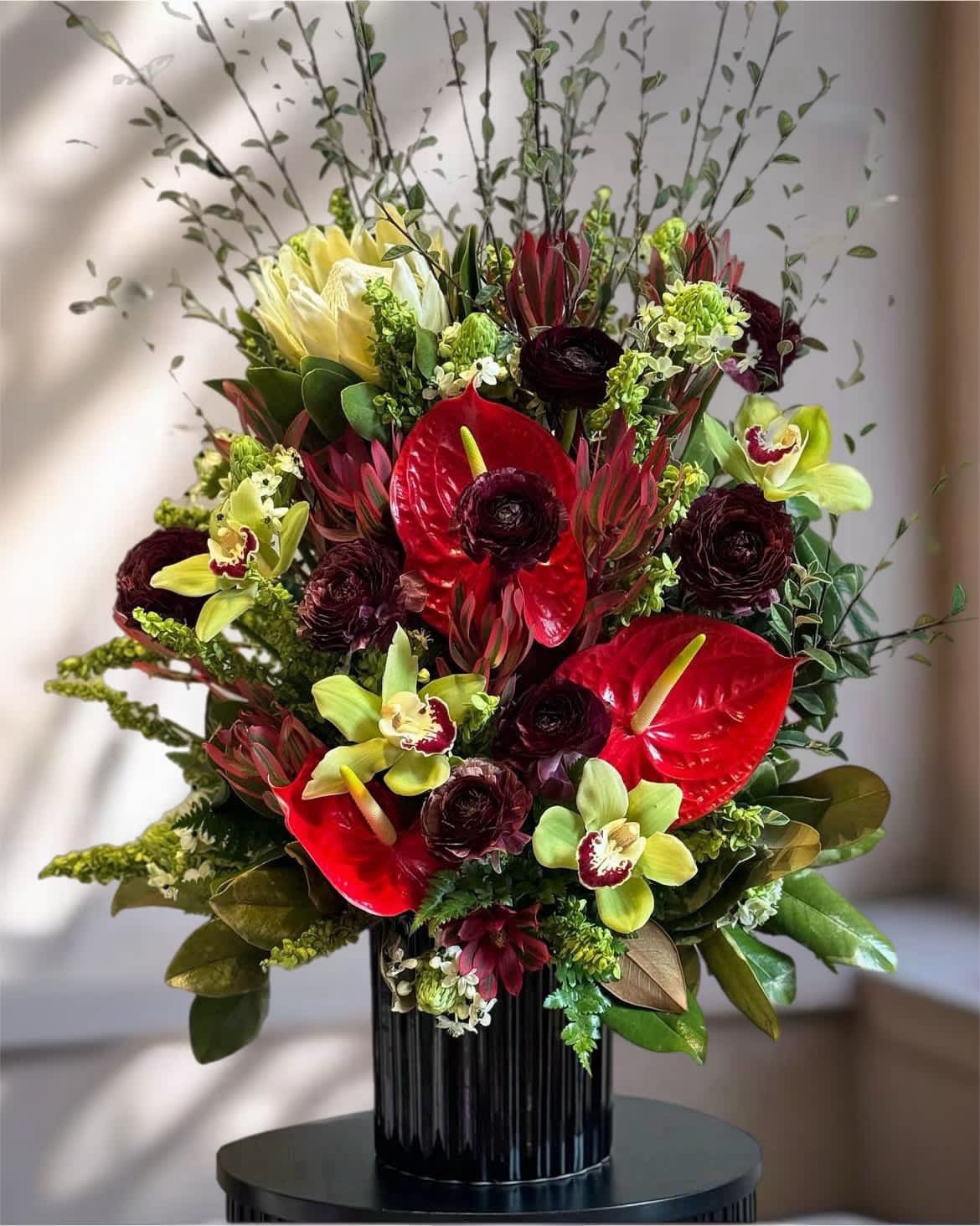 Red anthuriums and green orchids in a black vase