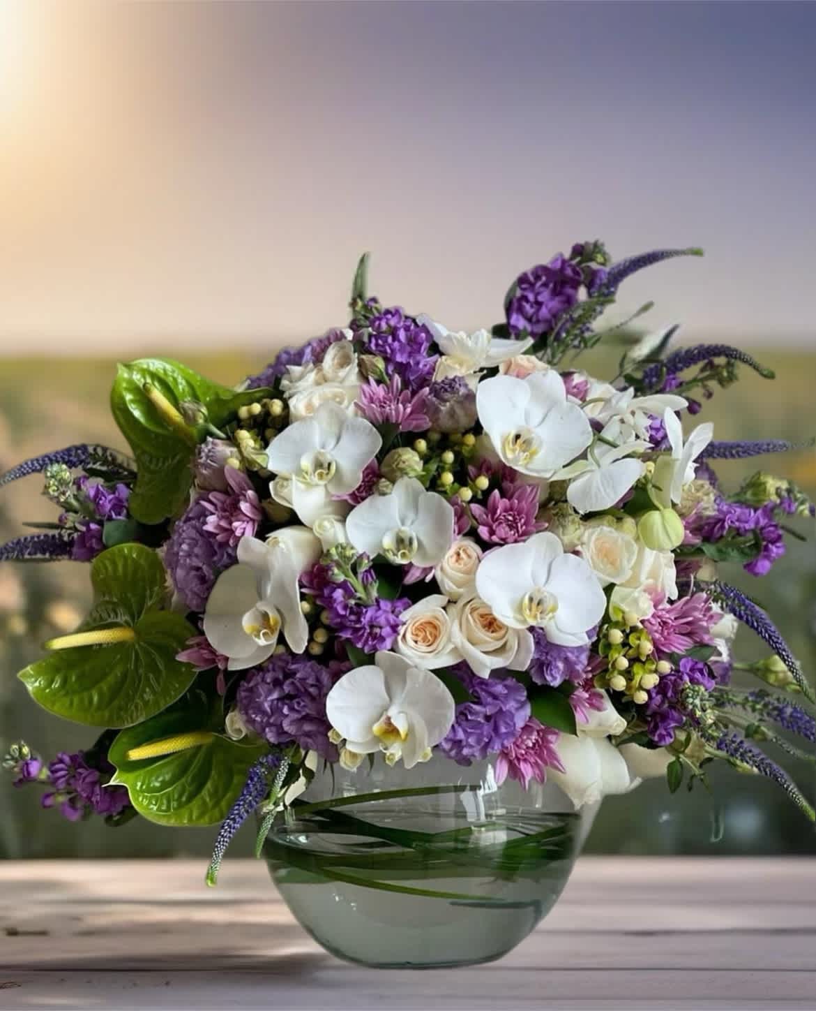 Purple and white floral arrangement in a glass bowl vase