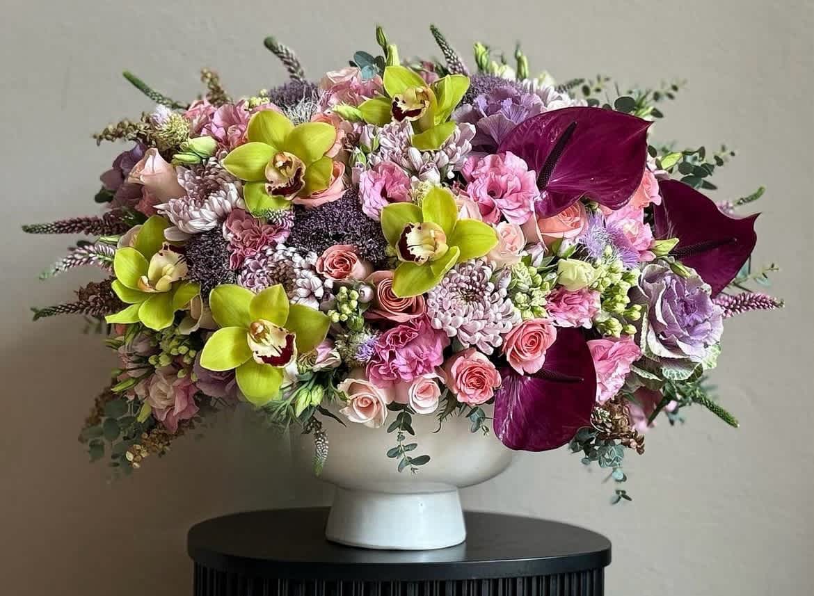 Large mixed bouquet in a white pedestal vase with pink, purple, and lime flowers
