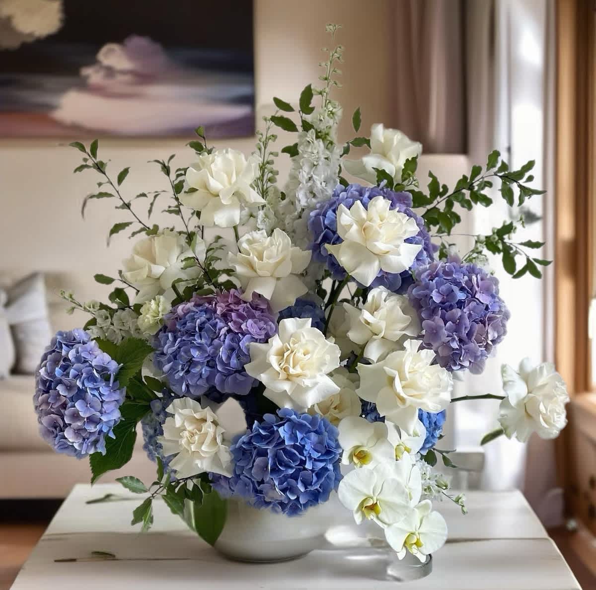 Blue hydrangeas and white orchids arranged in a white bowl vase