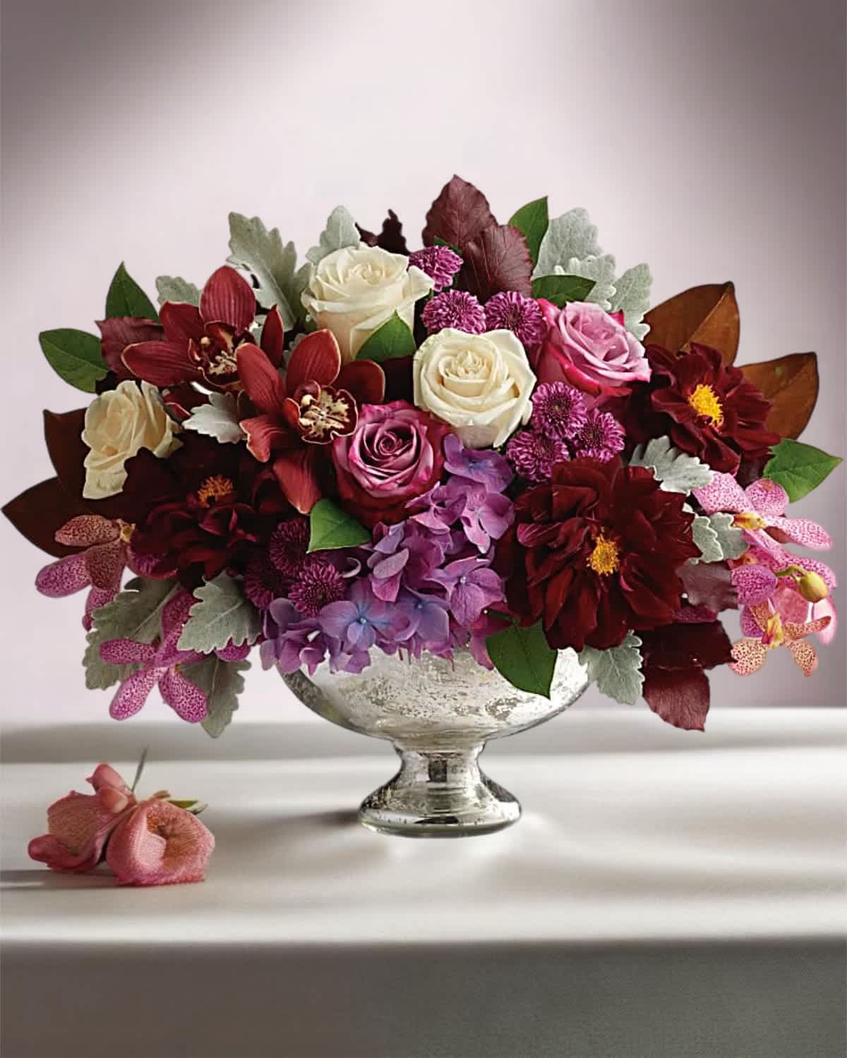 Mixed bouquet of roses, orchids, and purple blooms in a silver pedestal vase