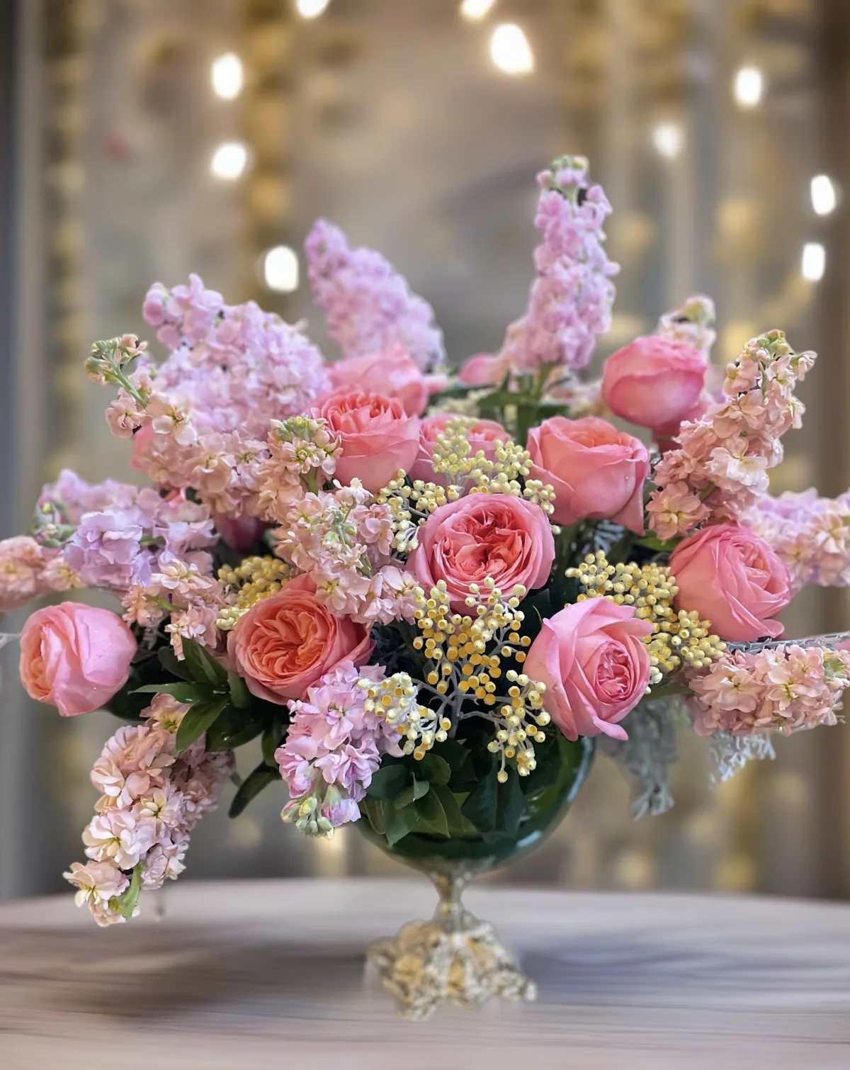 Pink roses and lilac flowers arranged in a glass compote vase
