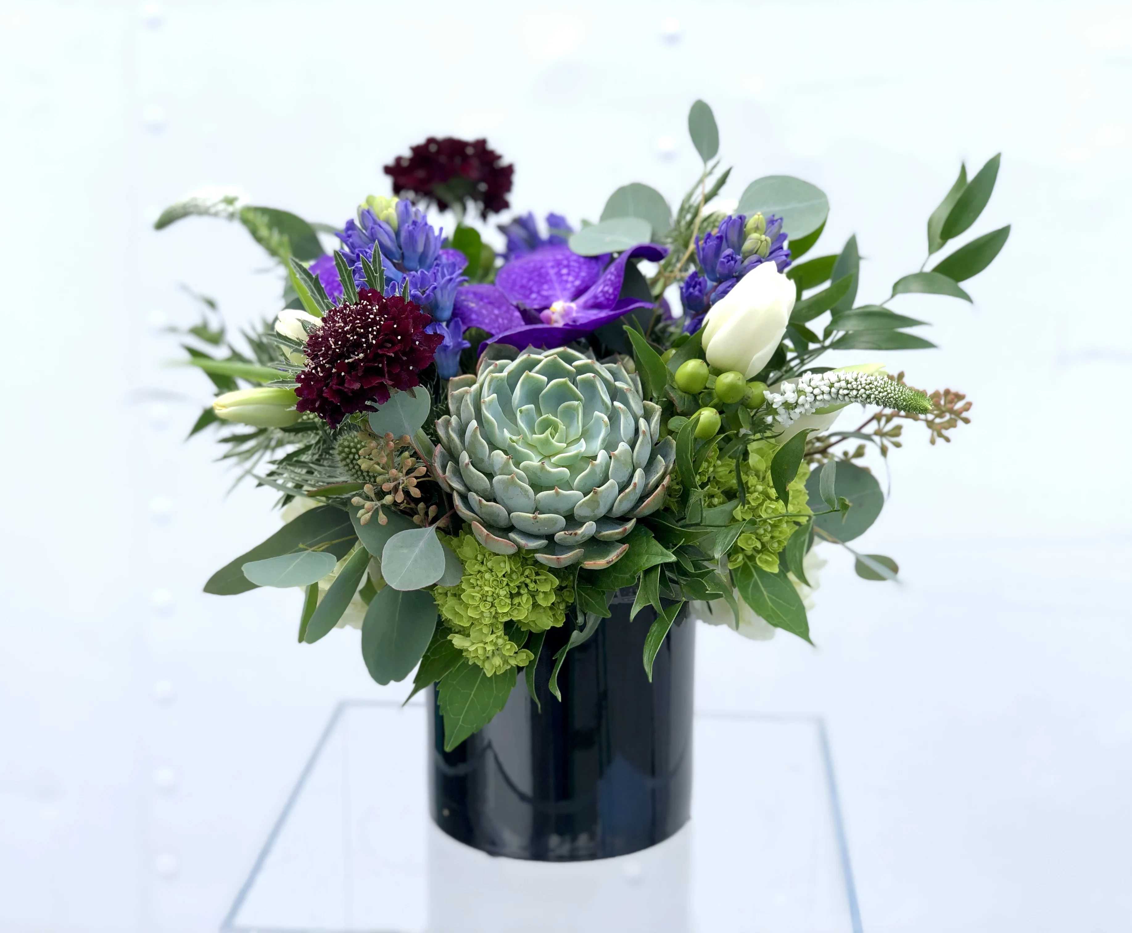 Purple and white floral arrangement with a succulent in a black vase