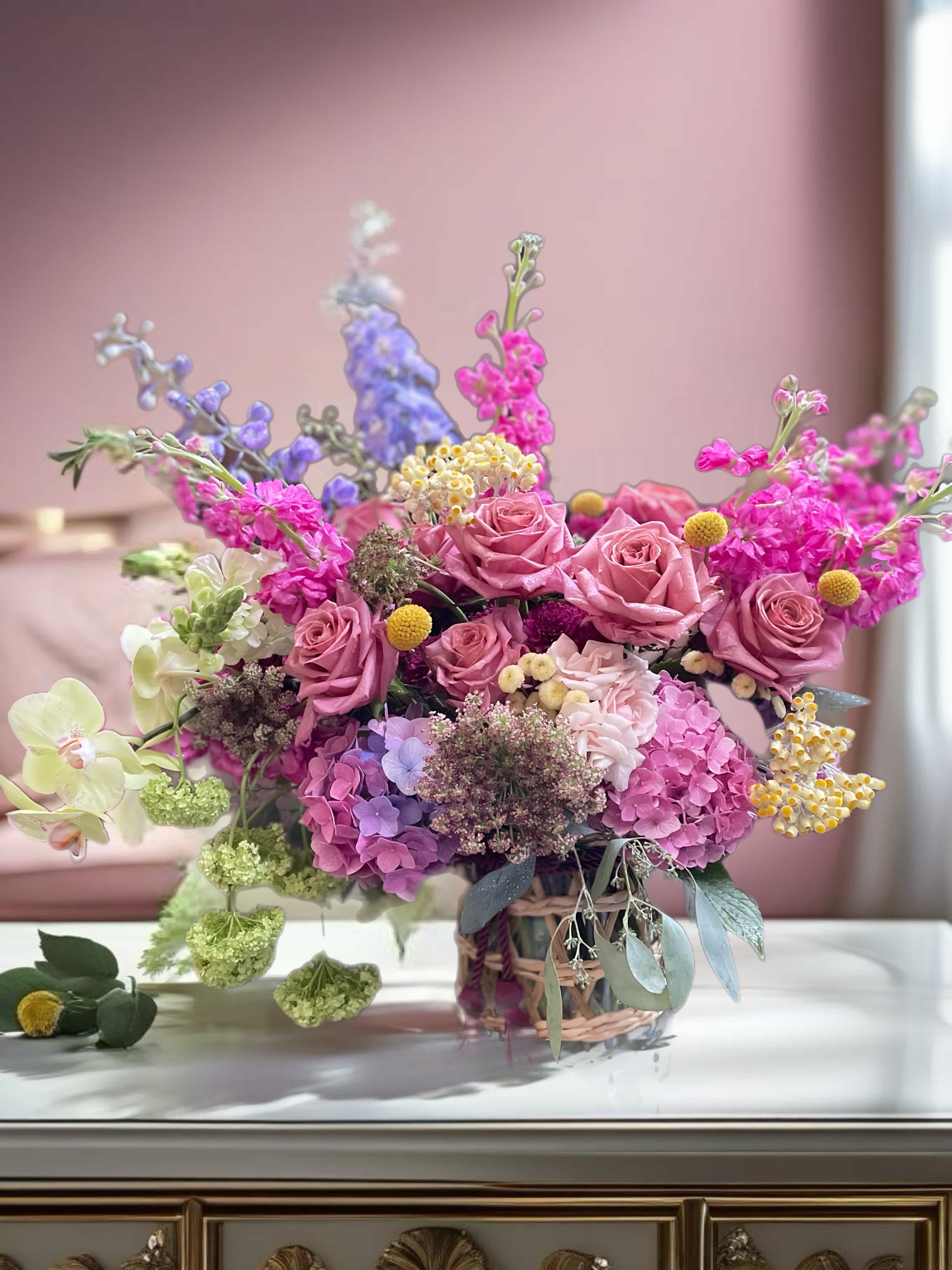 Pink roses and hydrangeas in a woven basket with purple and yellow accents