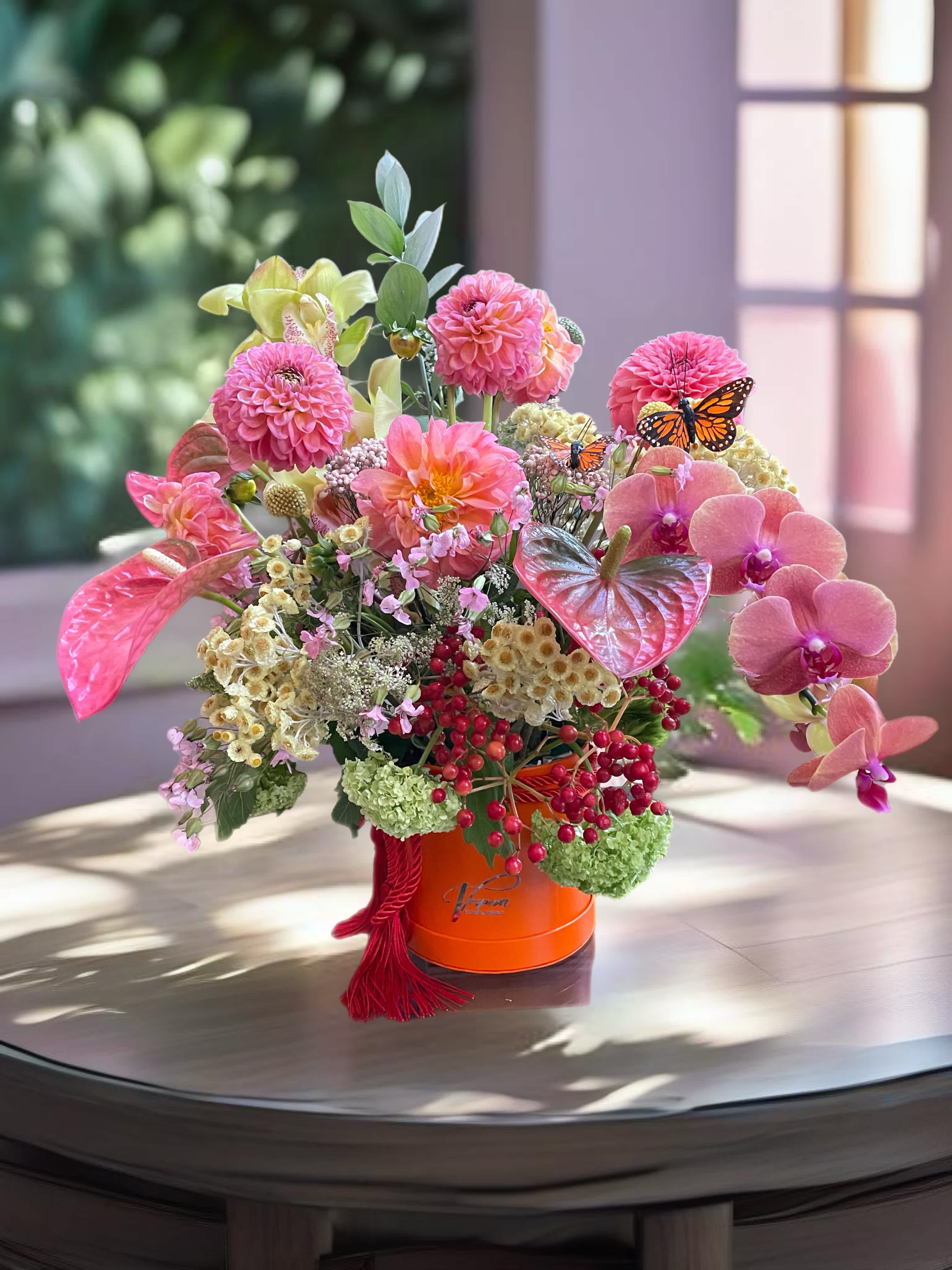 Pink and peach floral arrangement in an orange hatbox with butterfly accents