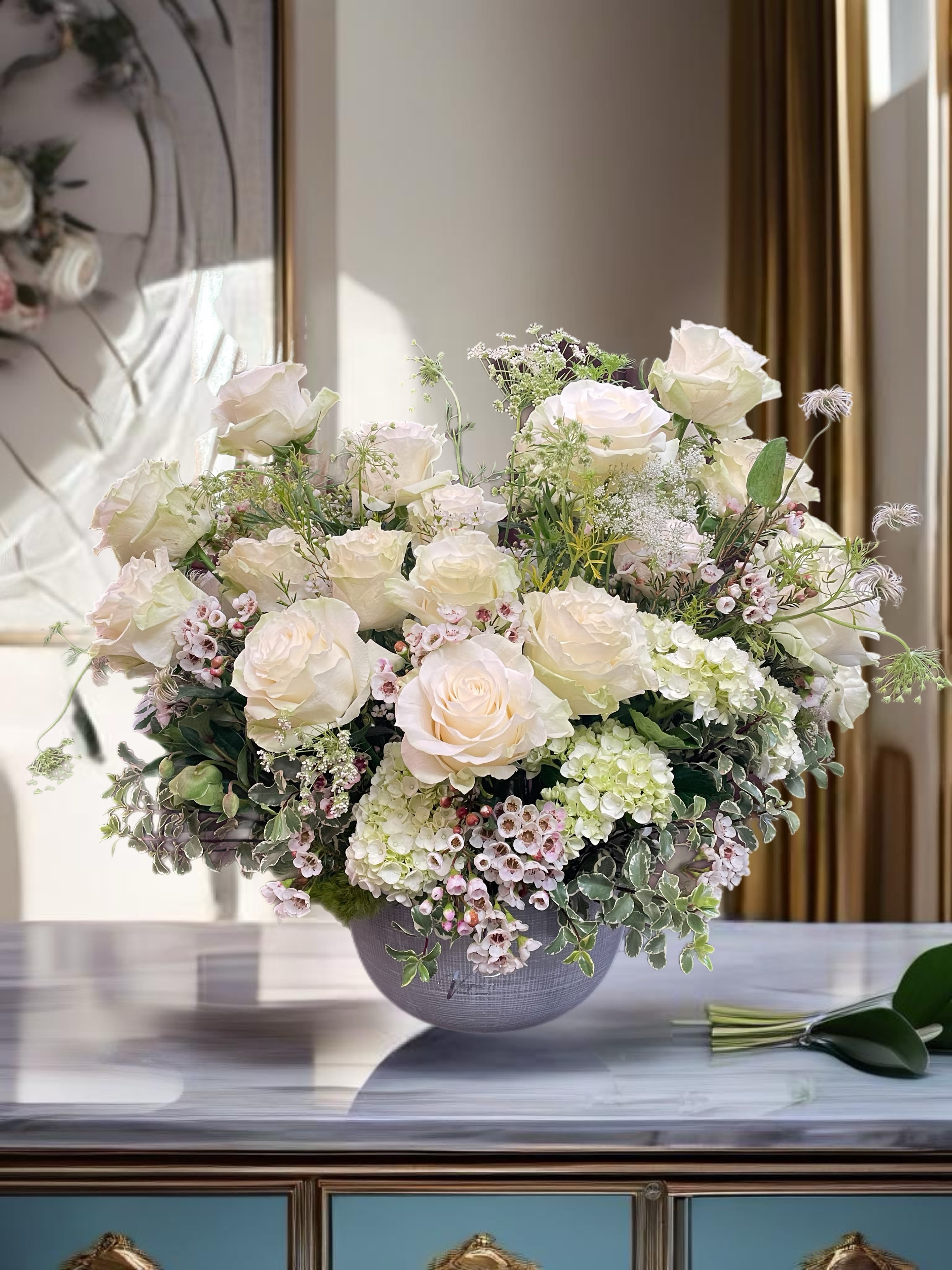 Cream rose arrangement in a gray vase with small pink filler flowers