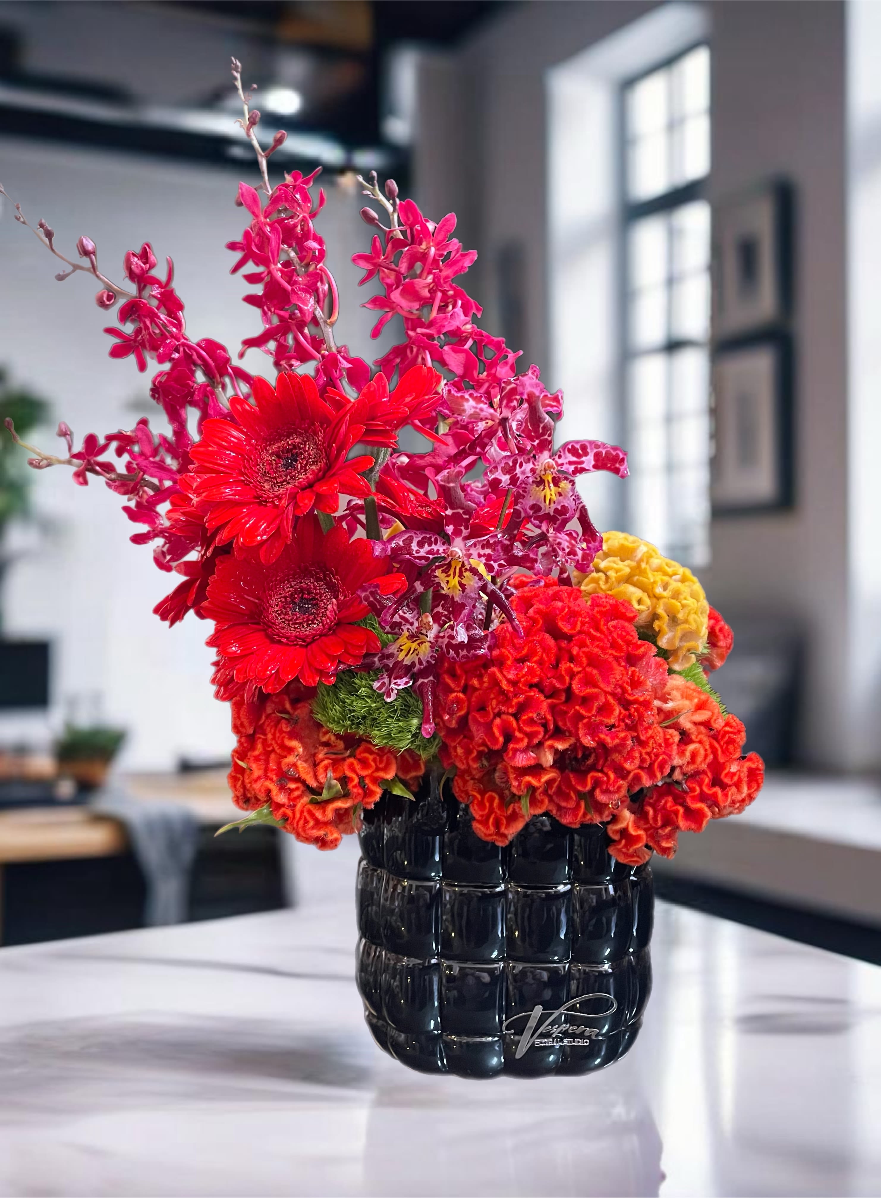 Bright red and pink floral arrangement in a black vase
